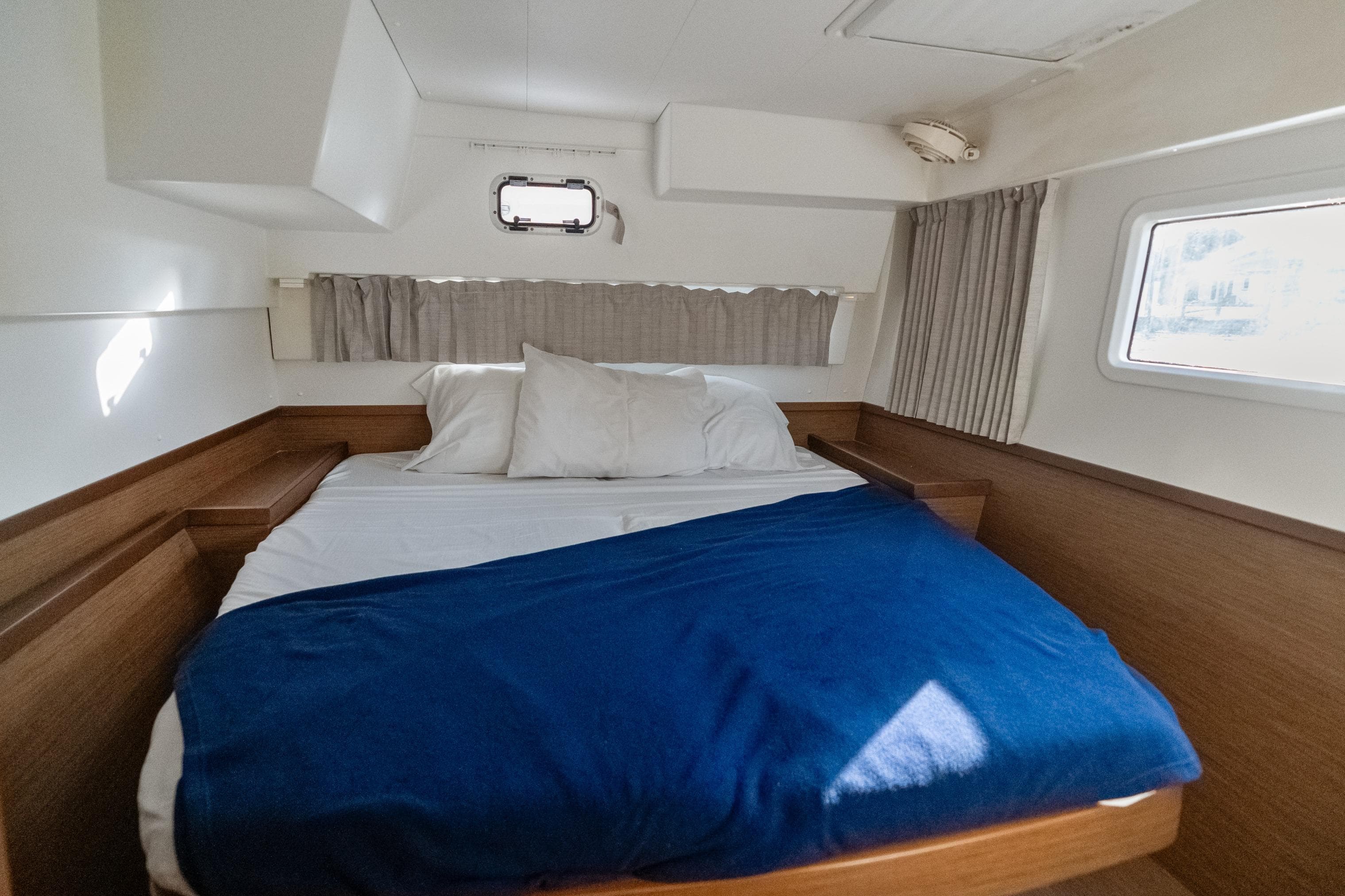 Cozy cabin interior of 2020 Lagoon 42 catamaran with bed and porthole window.