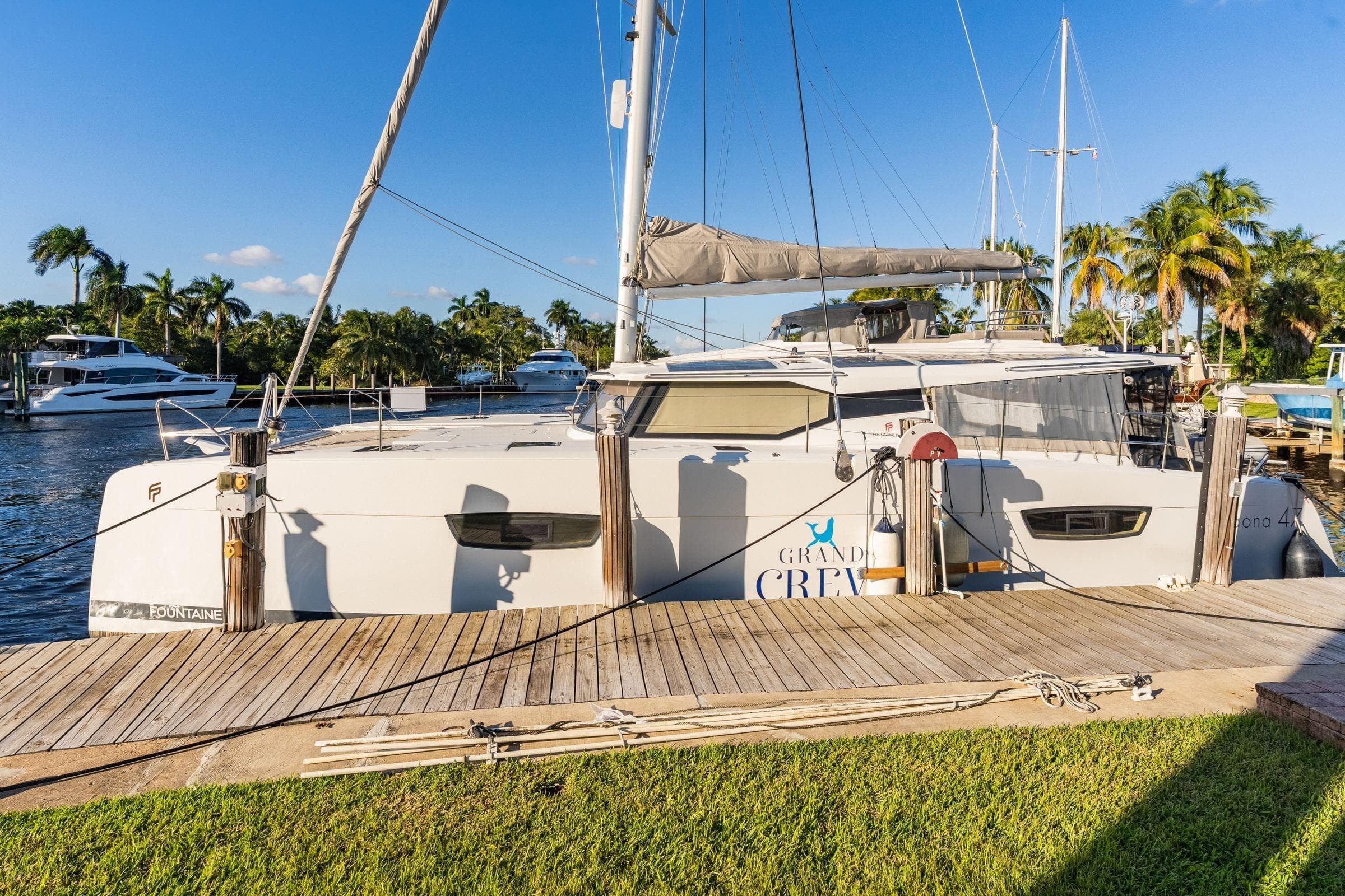 2019 Fountaine Pajot 47 catamaran docked, surrounded by palm trees and clear blue sky.