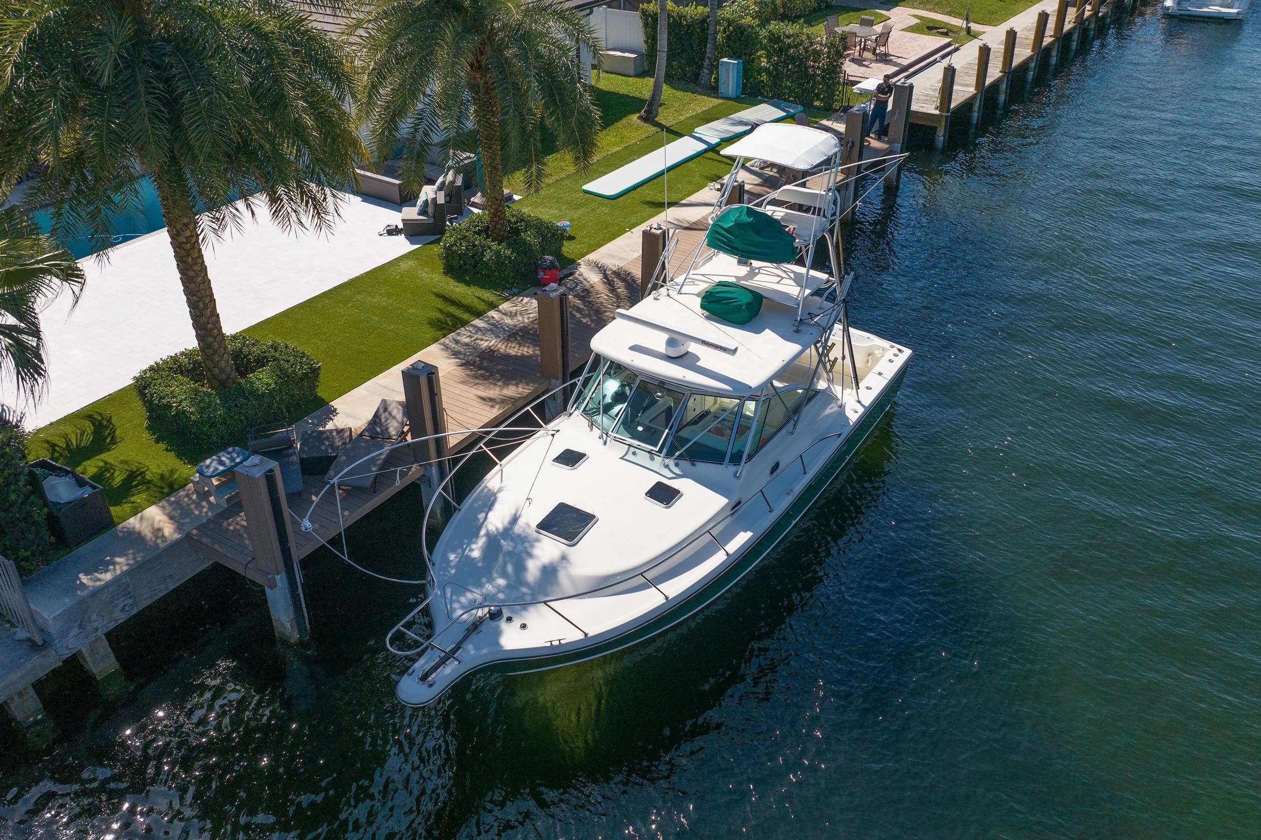 2000 Pursuit 3400 Express boat docked by palm trees and waterfront property.