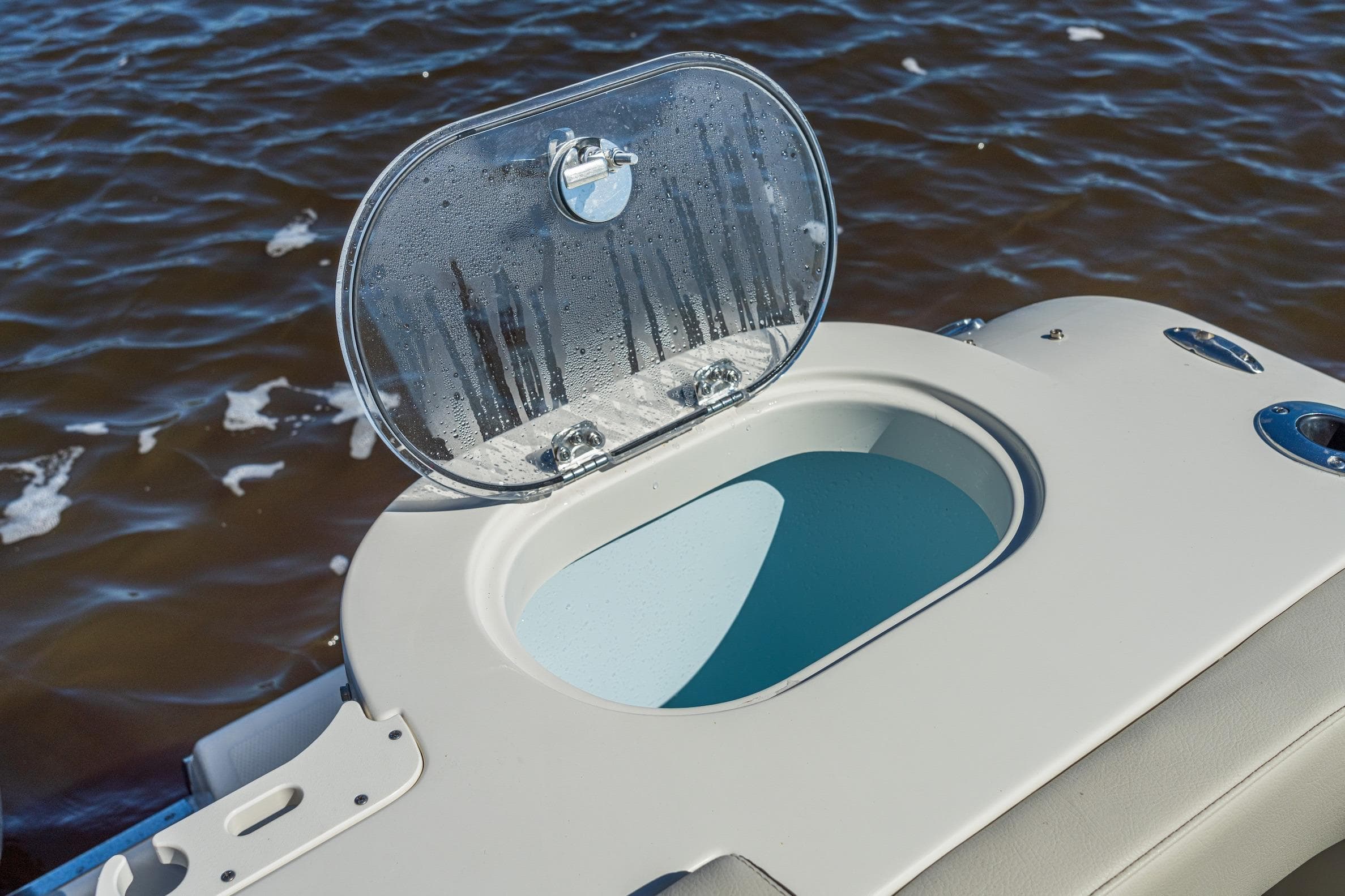 Open hatch on 2027 Sailfish 245 DC boat, revealing storage compartment by the water.
