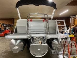 2025 Sweetwater 2286SB pontoon boat in a garage, rear view with ladder and canopy.