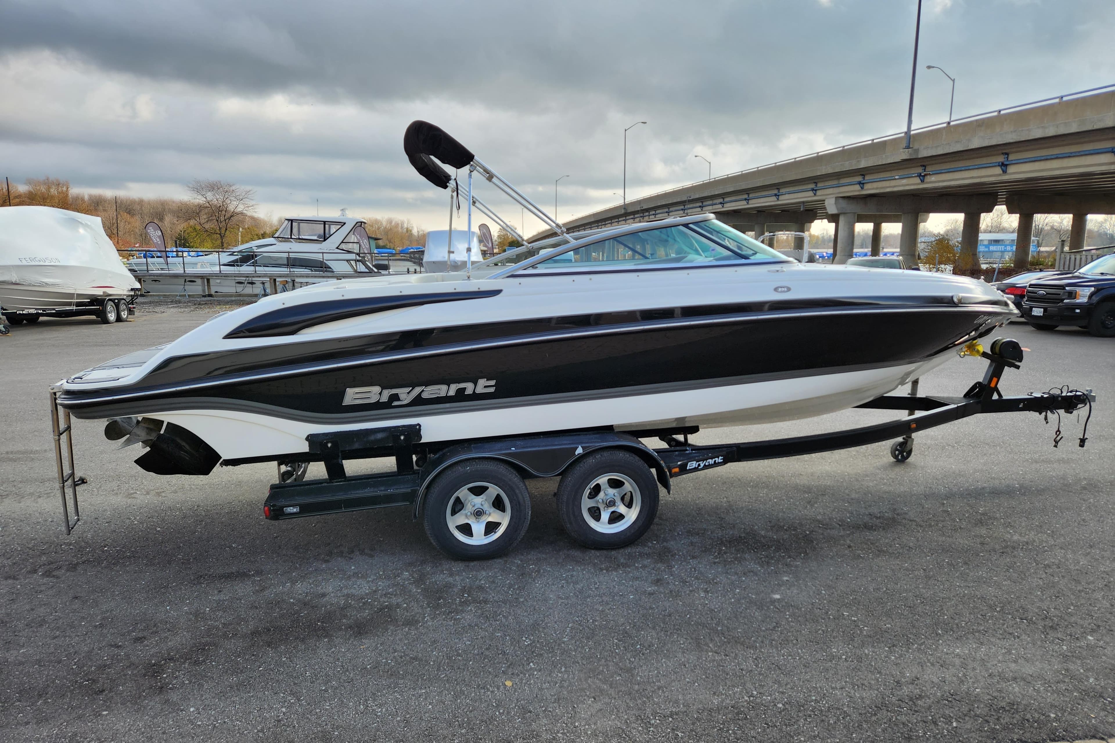 2009 Bryant 233 boat on trailer, parked outdoors under cloudy sky.