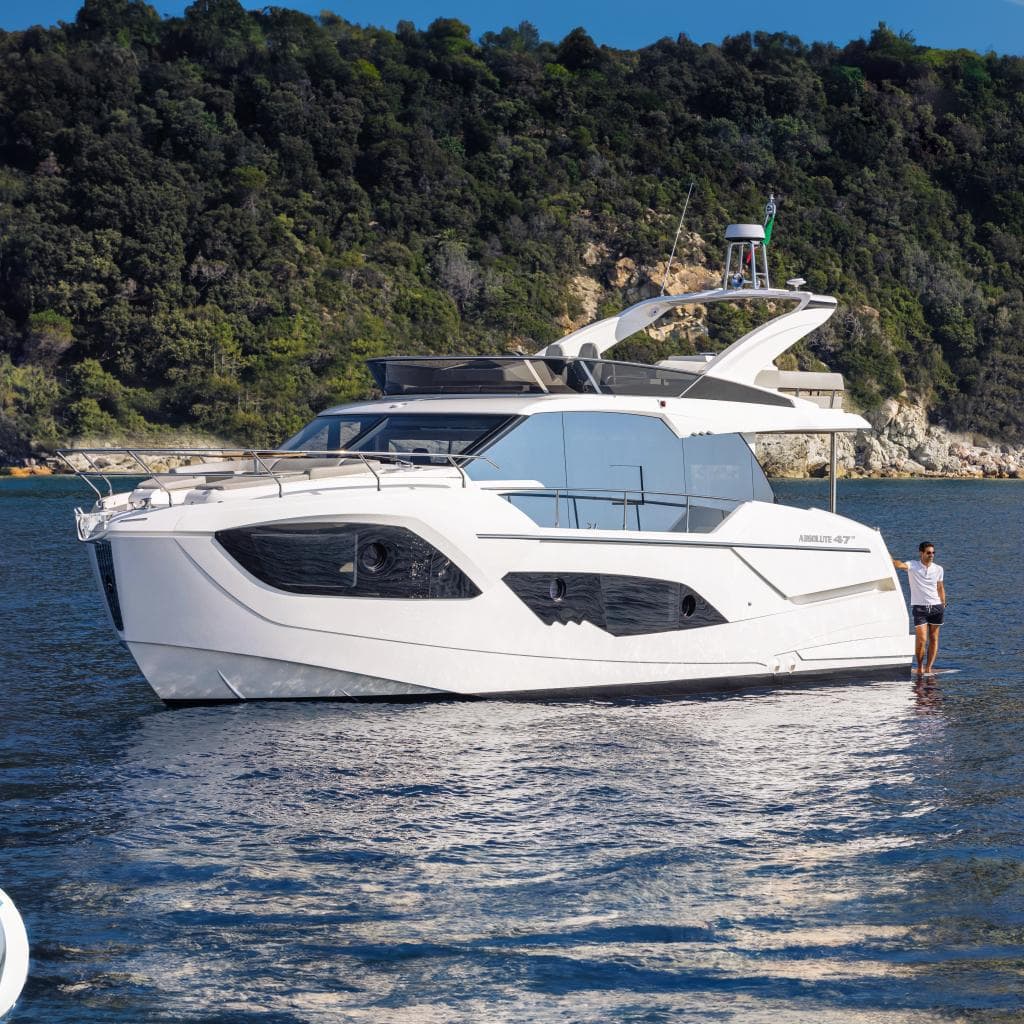 2025 Absolute 47 Fly yacht on serene waters with lush green backdrop.