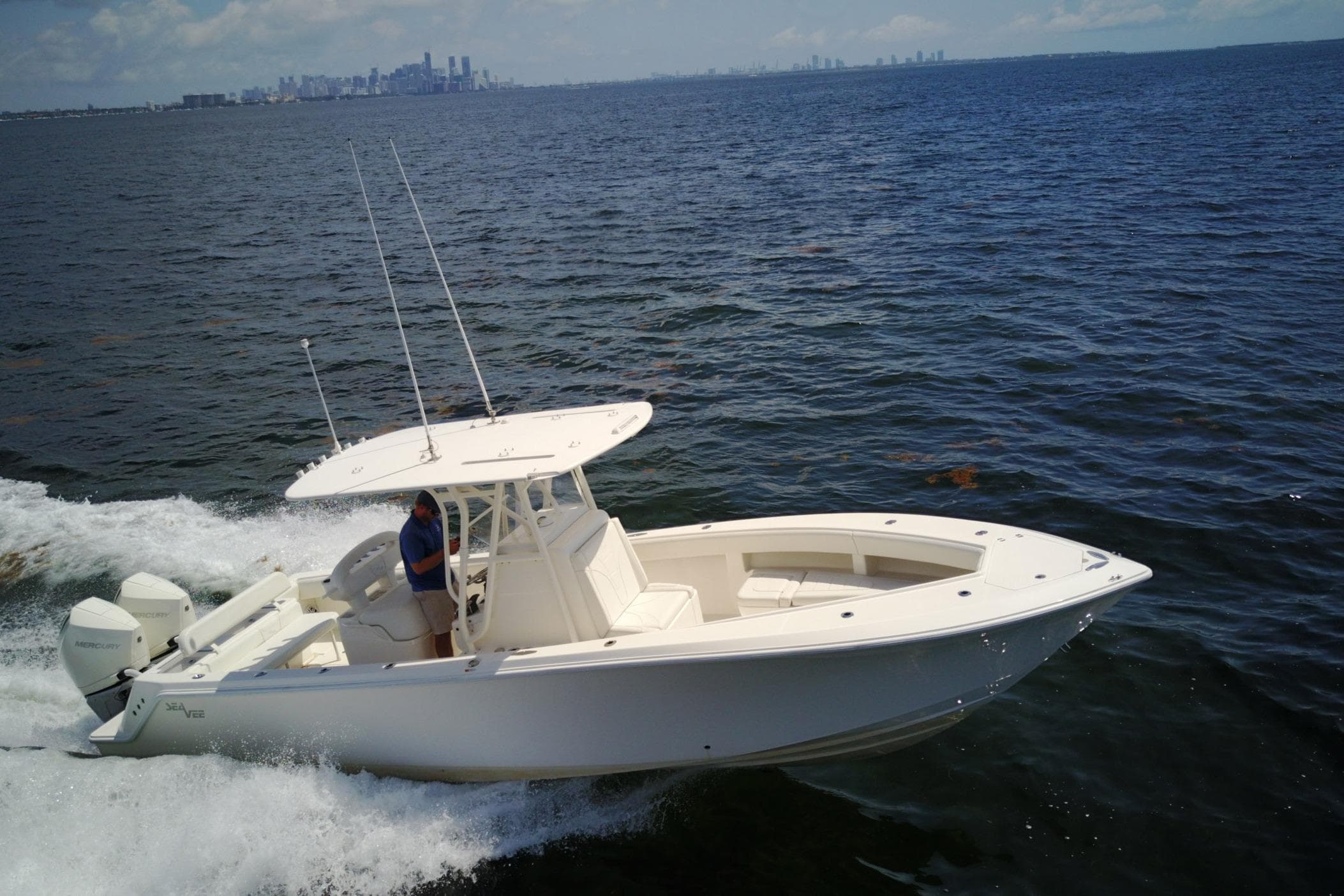 2023 SeaVee 290B boat cruising on open water with city skyline in background.