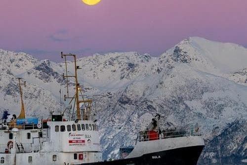 Custom 1967 North Sea Trawler against snowy mountains and pink sky at sunset.