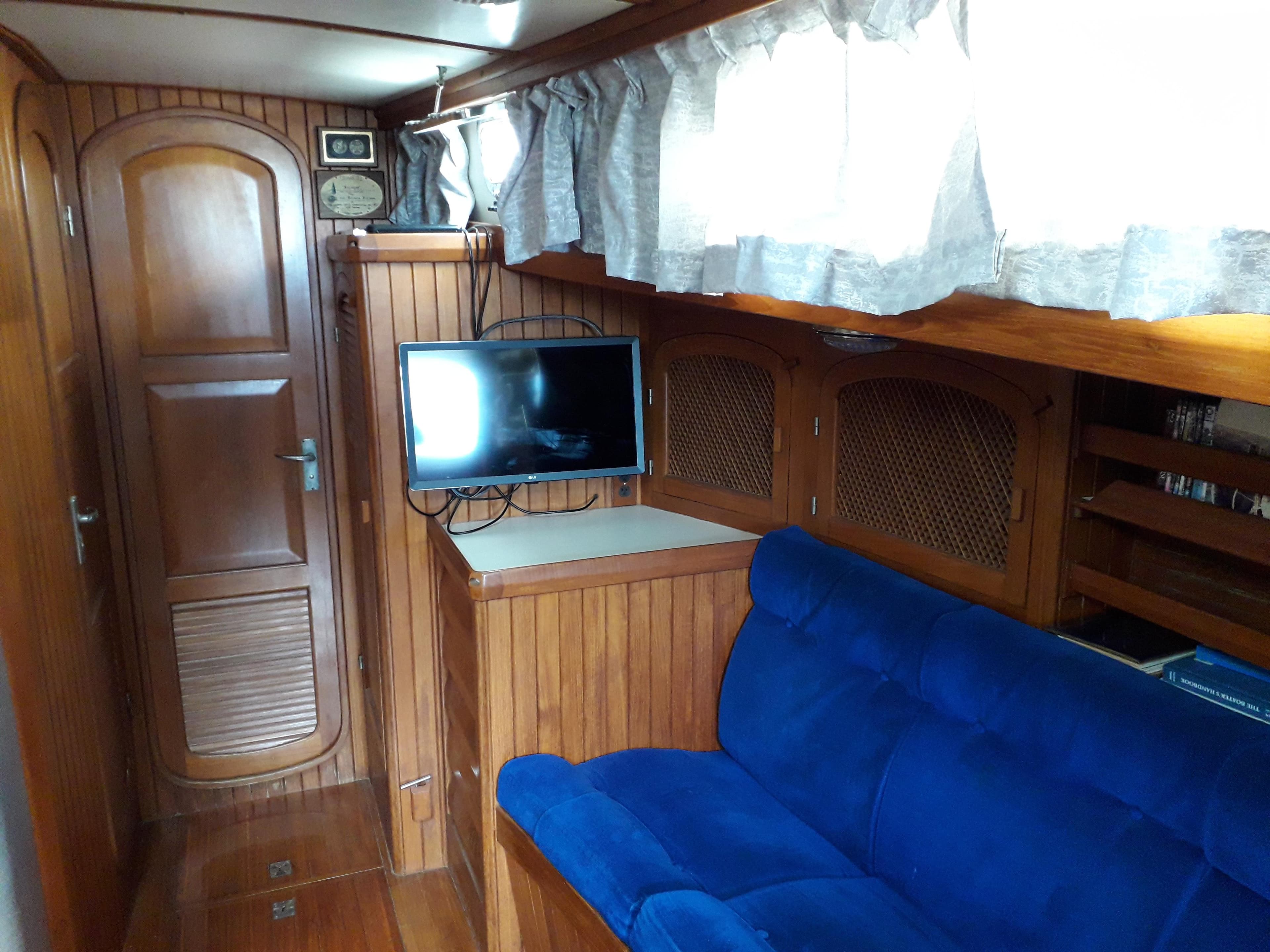 Interior of 1986 Slocum 43 Cutter with wood paneling, blue sofa, and mounted TV.