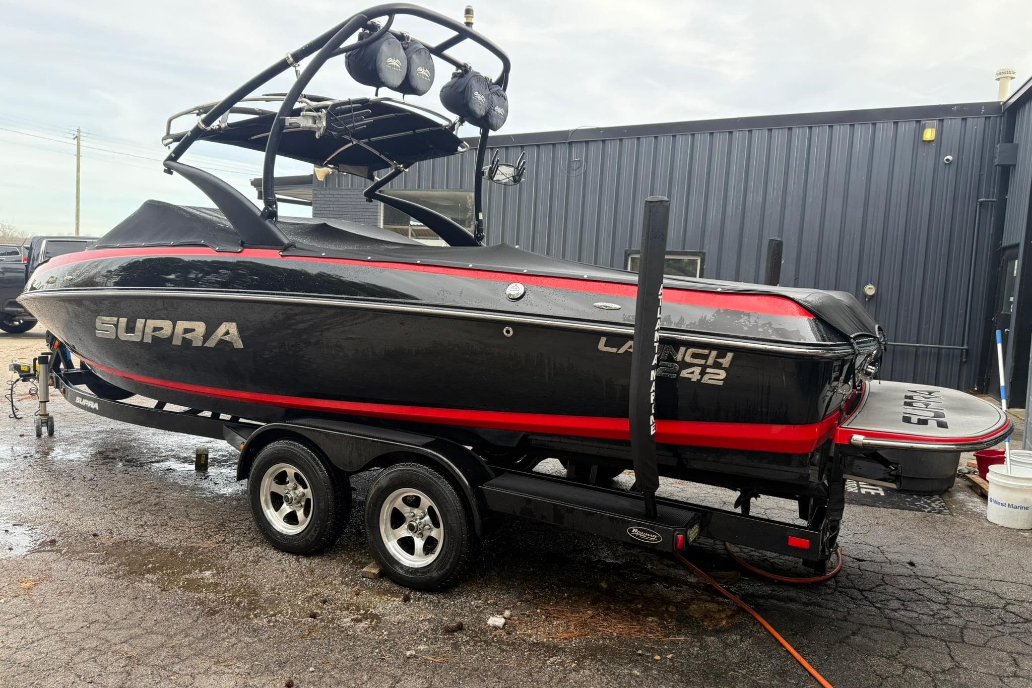 2011 Supra Launch 242 boat on trailer, black with red accents, parked outdoors.