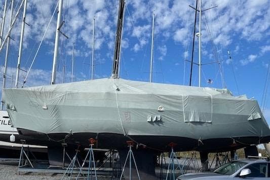 Covered C&C 121 sailboat from 2002 on stands, under a blue sky.