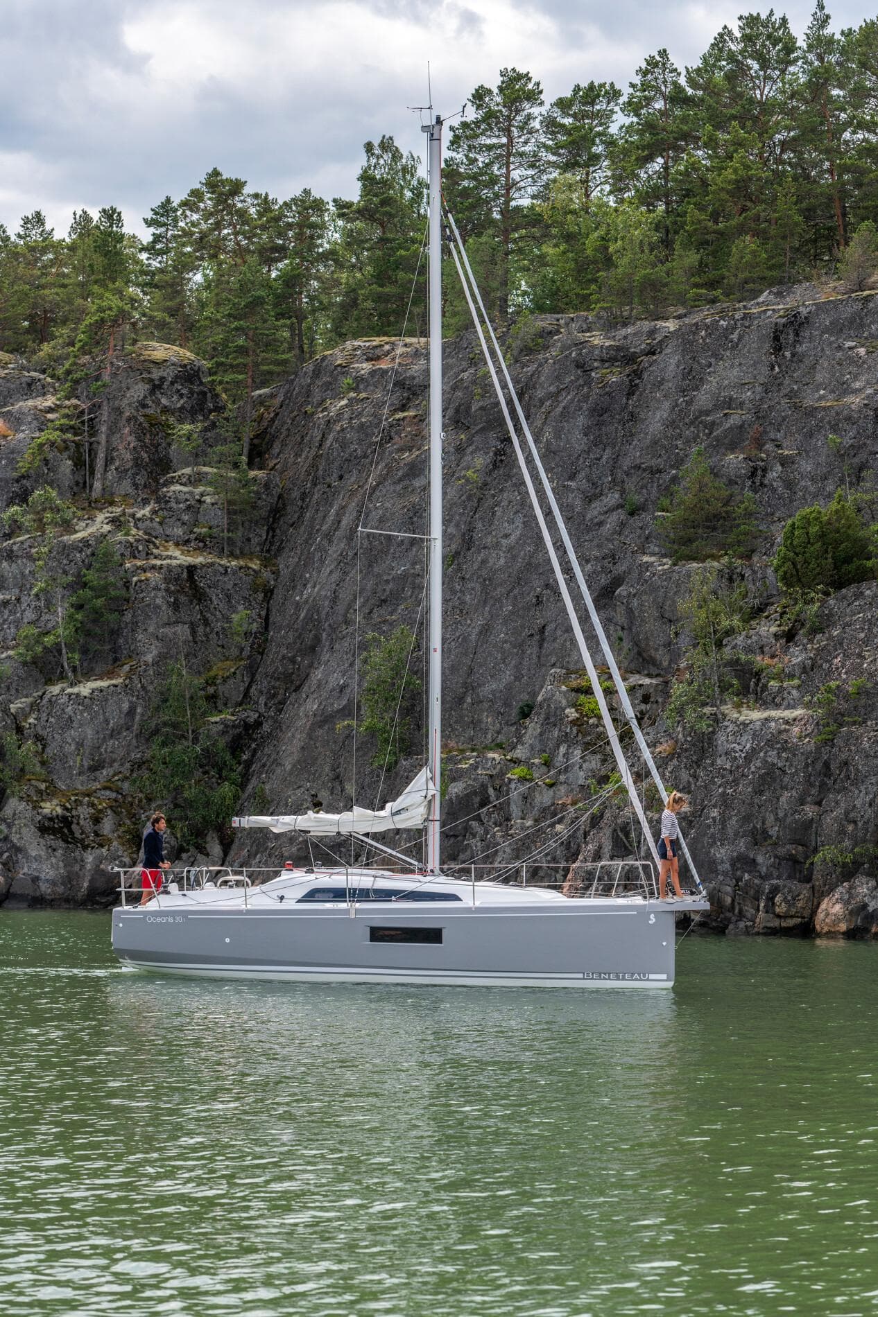 2024 Beneteau Oceanis 30.1 sailboat cruising near rocky cliffs and lush greenery.
