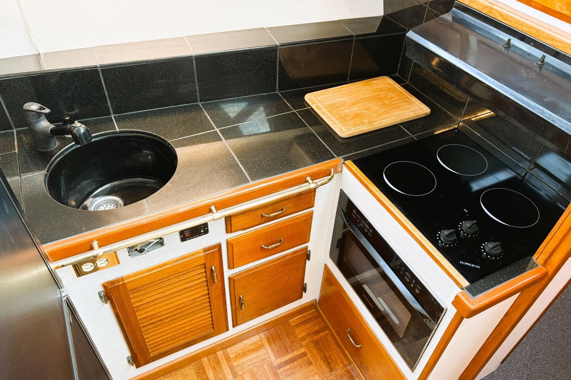 1980 Tollycraft 34 Sedan kitchen with black countertops, stove, and wooden cabinetry.