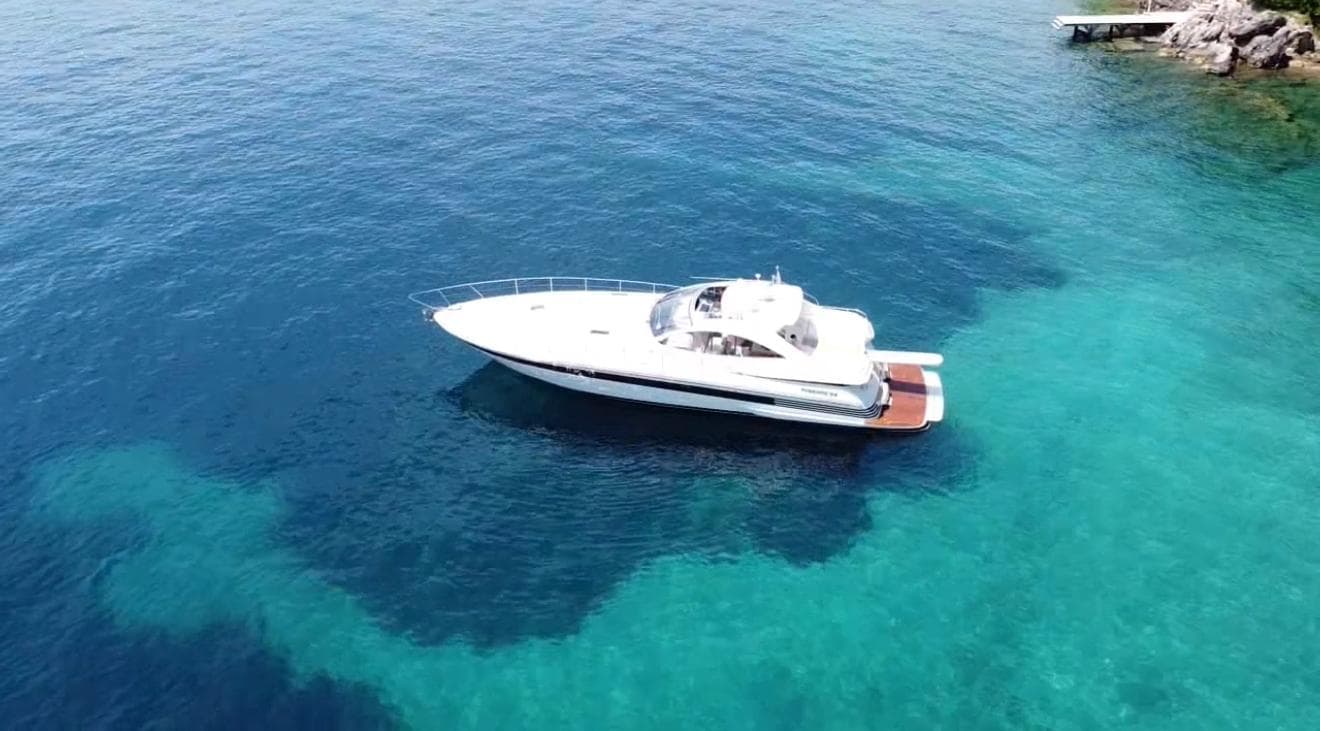 2004 Pershing 54 yacht on clear blue water near rocky shoreline.