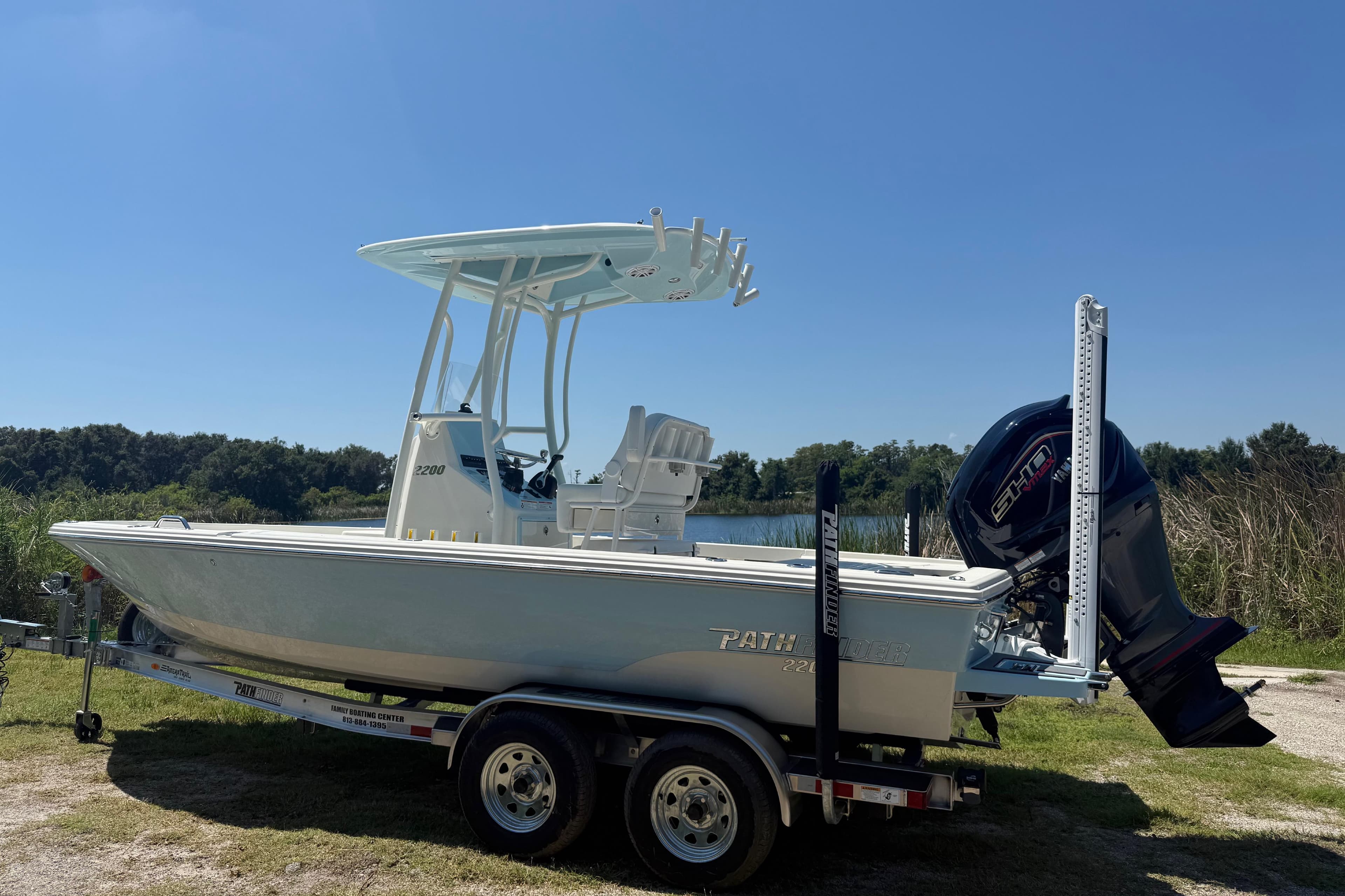 2026 Pathfinder 2200 TRS boat on trailer, parked near a lake under clear blue sky.
