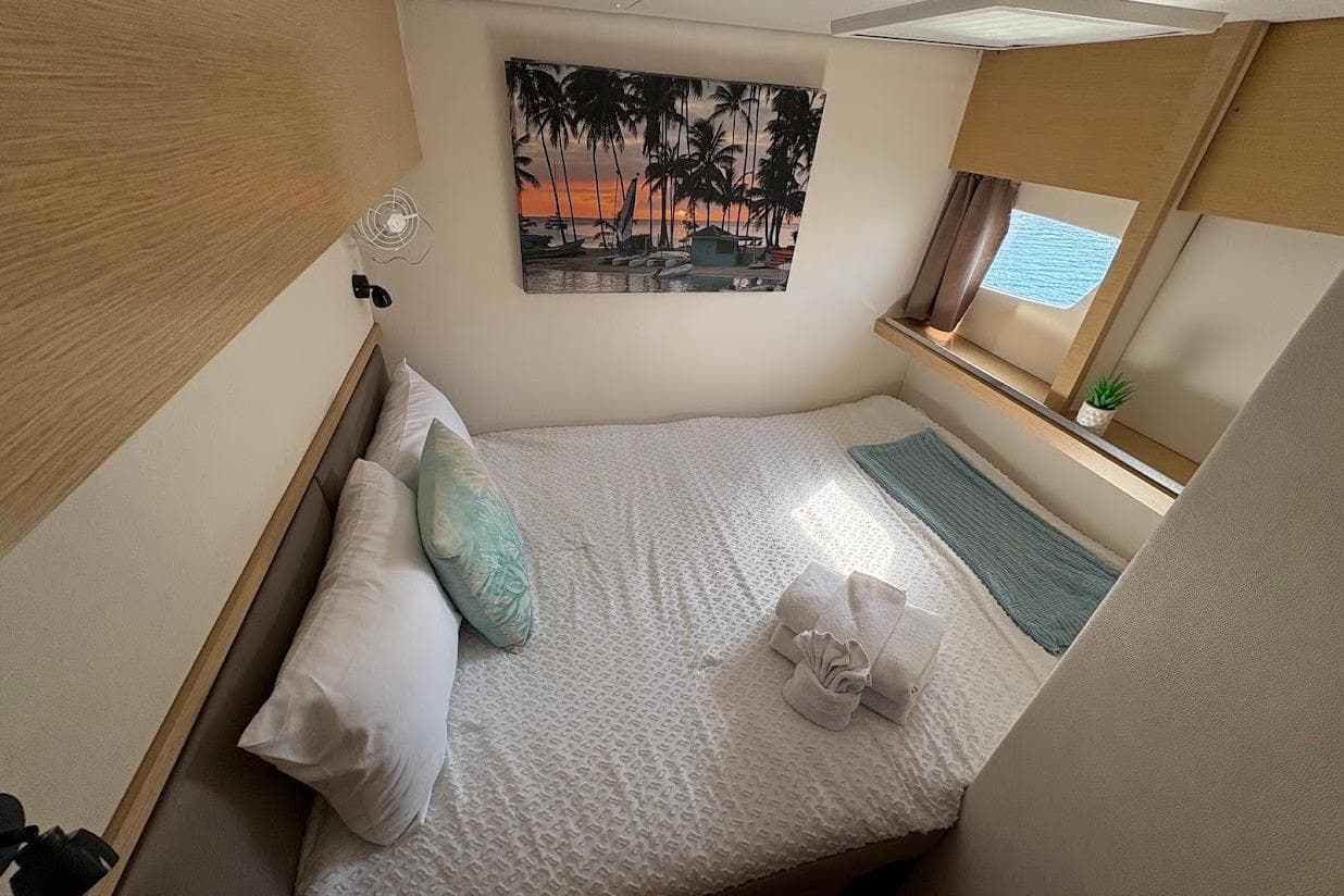 Cozy cabin interior of 2015 Fountaine Pajot SABA 50 with bed, window, and tropical decor.