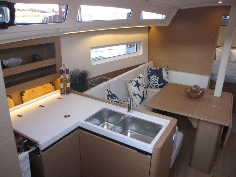 Modern interior of 2024 Jeanneau 380 sailboat with kitchen and dining area.