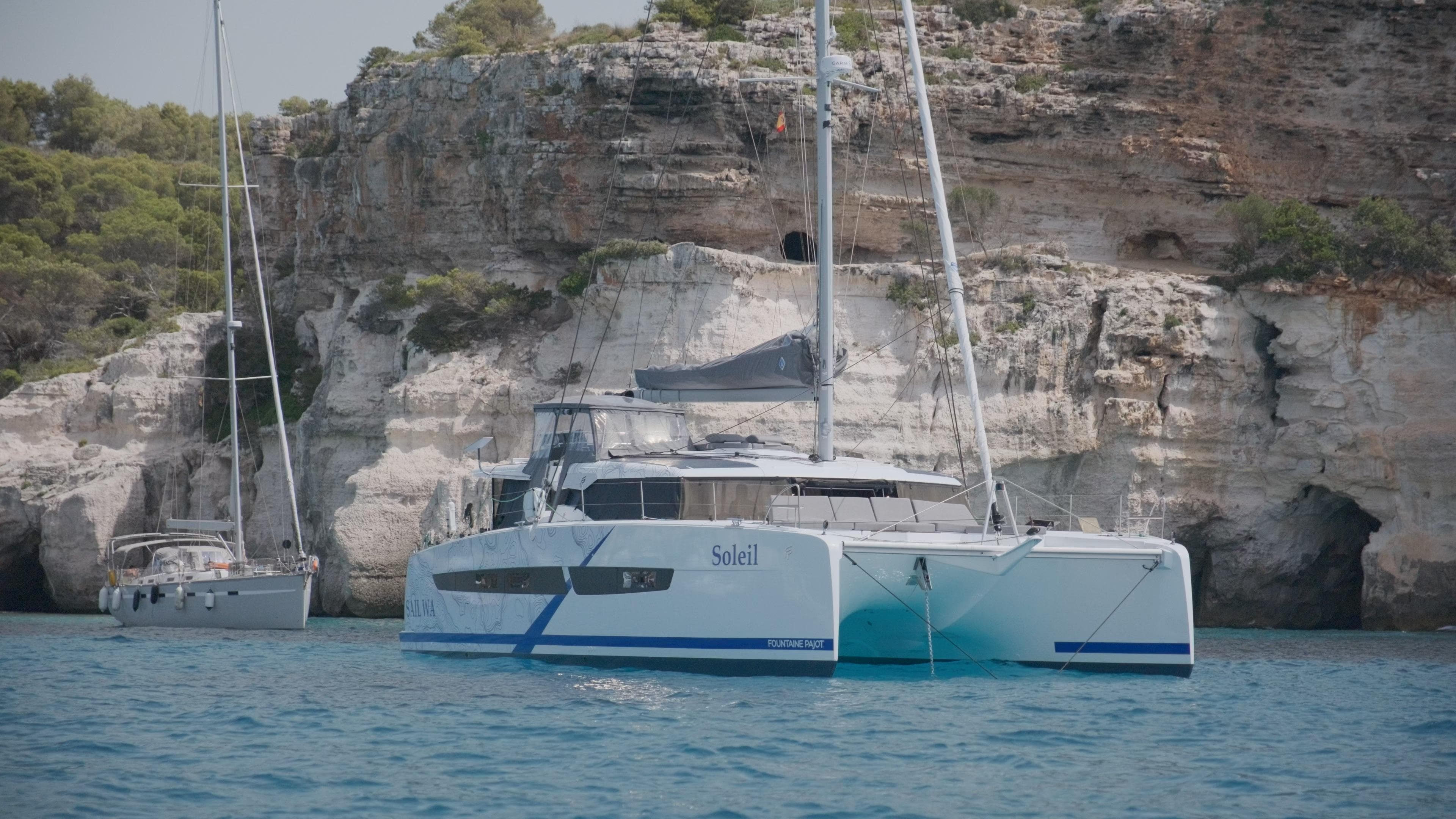 2023 Fountaine Pajot Catamaran Aura 51 anchored near rocky cliffs.