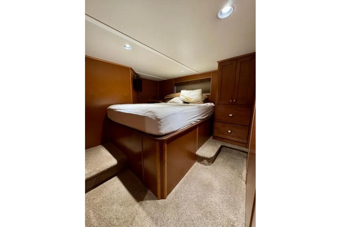 Cozy bedroom interior in 2012 Bravada Helios Trip #7 houseboat, featuring a raised bed and wooden cabinetry.