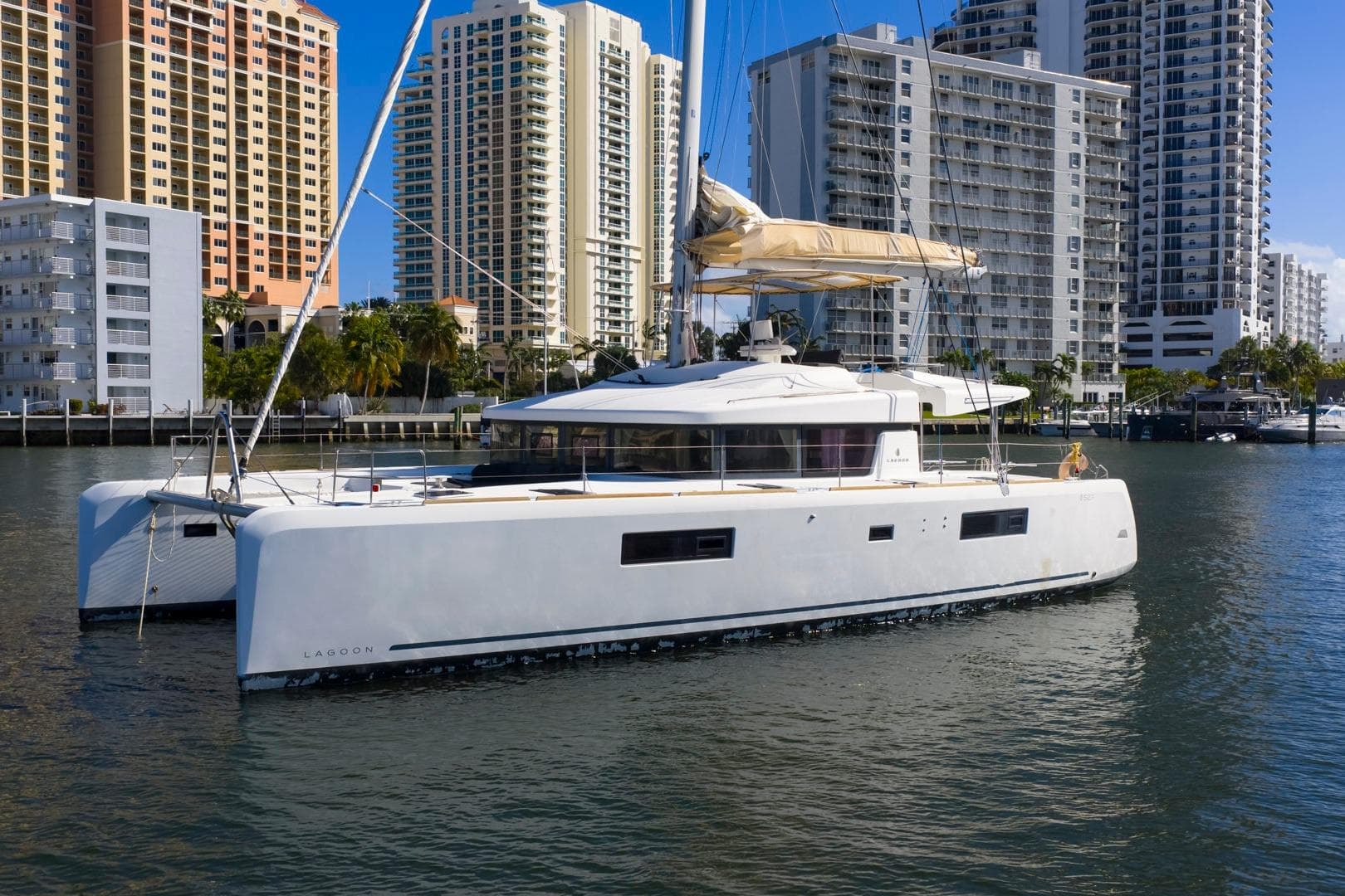 2021 Lagoon 52 F catamaran sailing near urban waterfront with high-rise buildings.