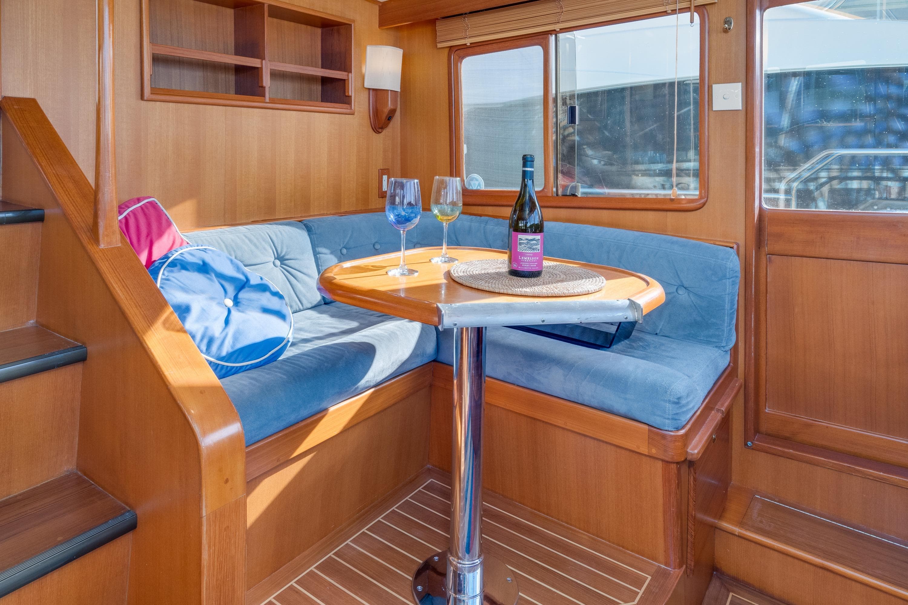 Cozy interior of 2001 Fleming 55 Pilothouse with blue seating and wine on table.