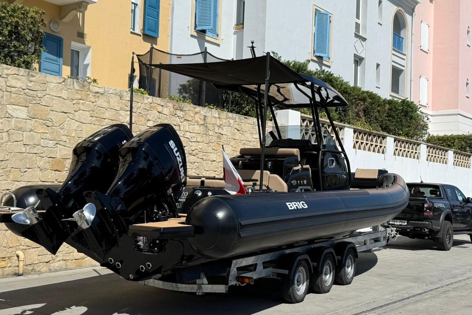 2024 Brig Eagle boat on trailer with dual Suzuki engines, parked near colorful buildings.