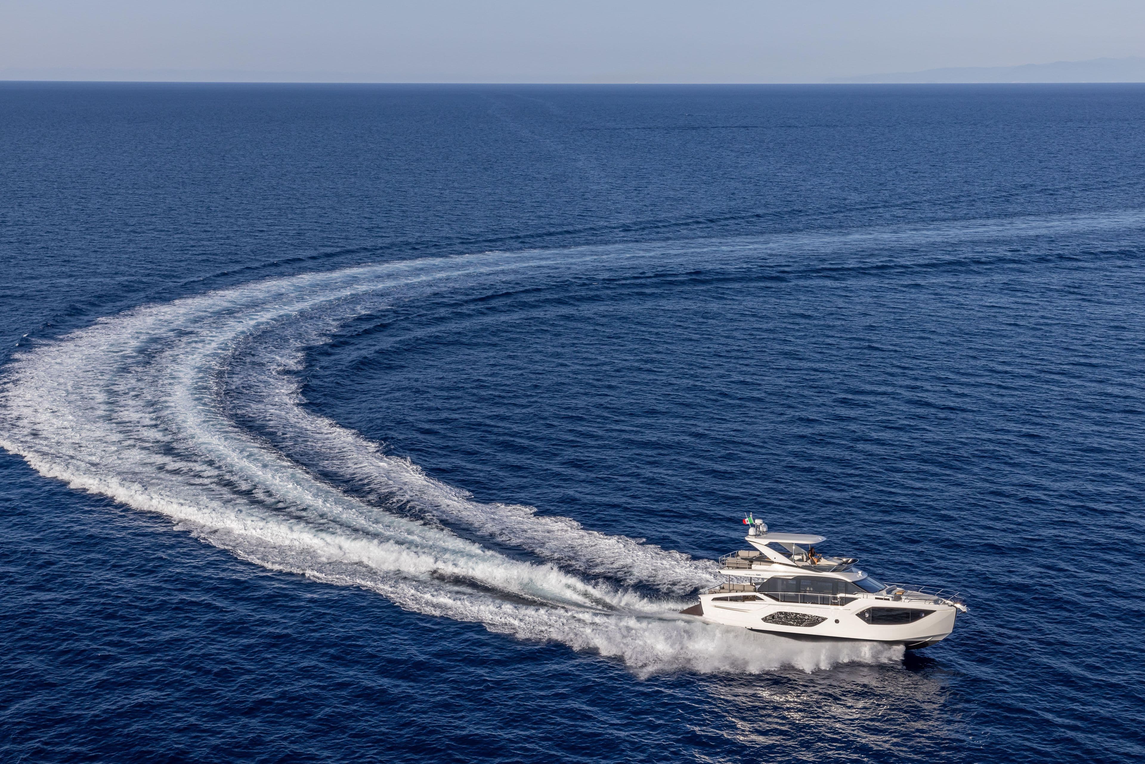 2025 Absolute 56 FLY yacht cruising on open sea, leaving a curved wake.