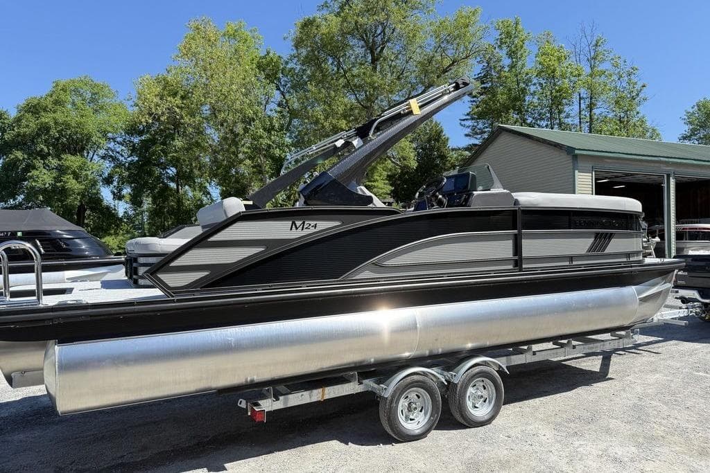 2026 Bennington M Swingback 24 MSB pontoon boat on trailer, surrounded by trees.