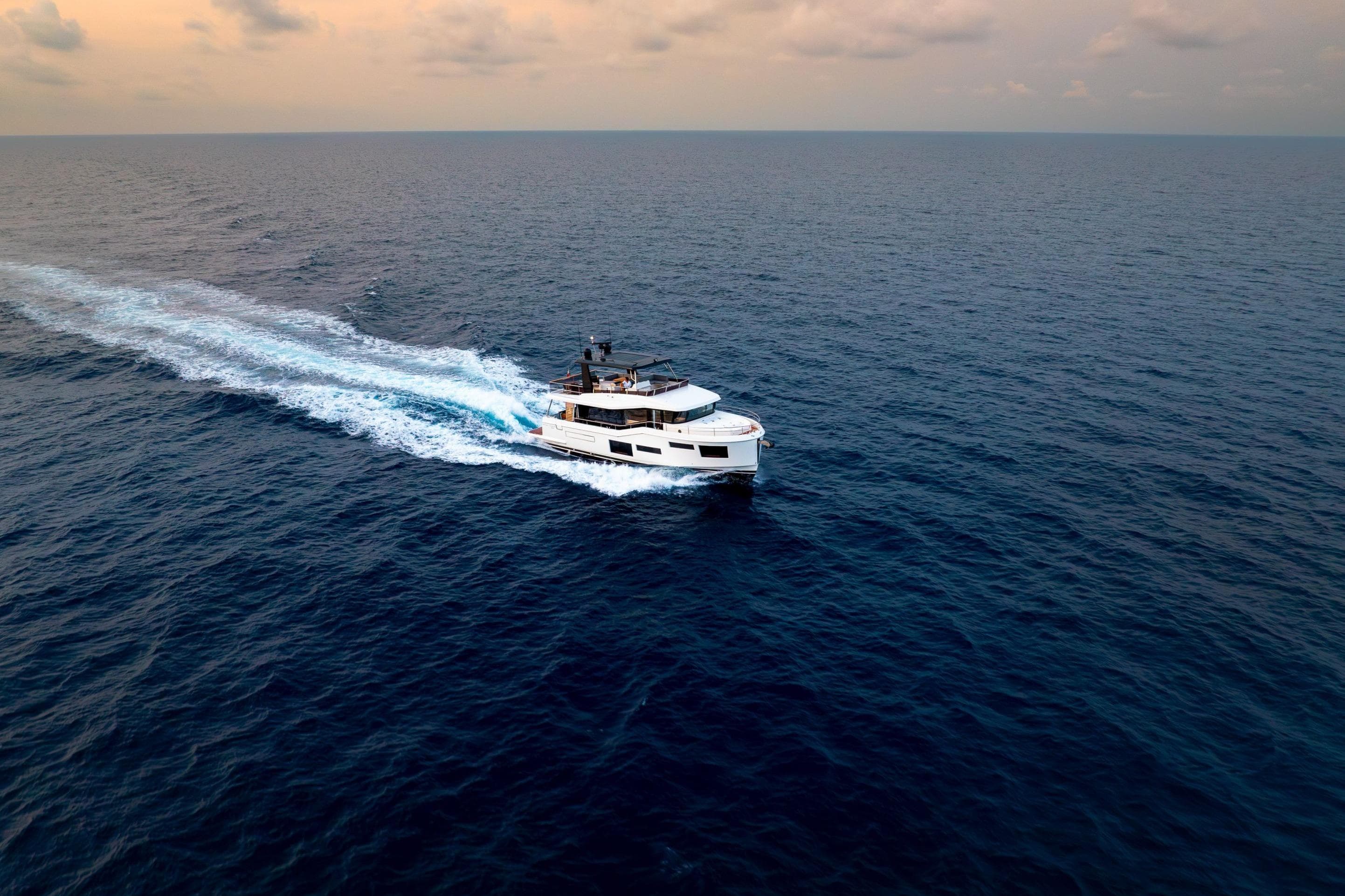 2025 Beneteau Grand Trawler 63 cruising on open sea at sunset.