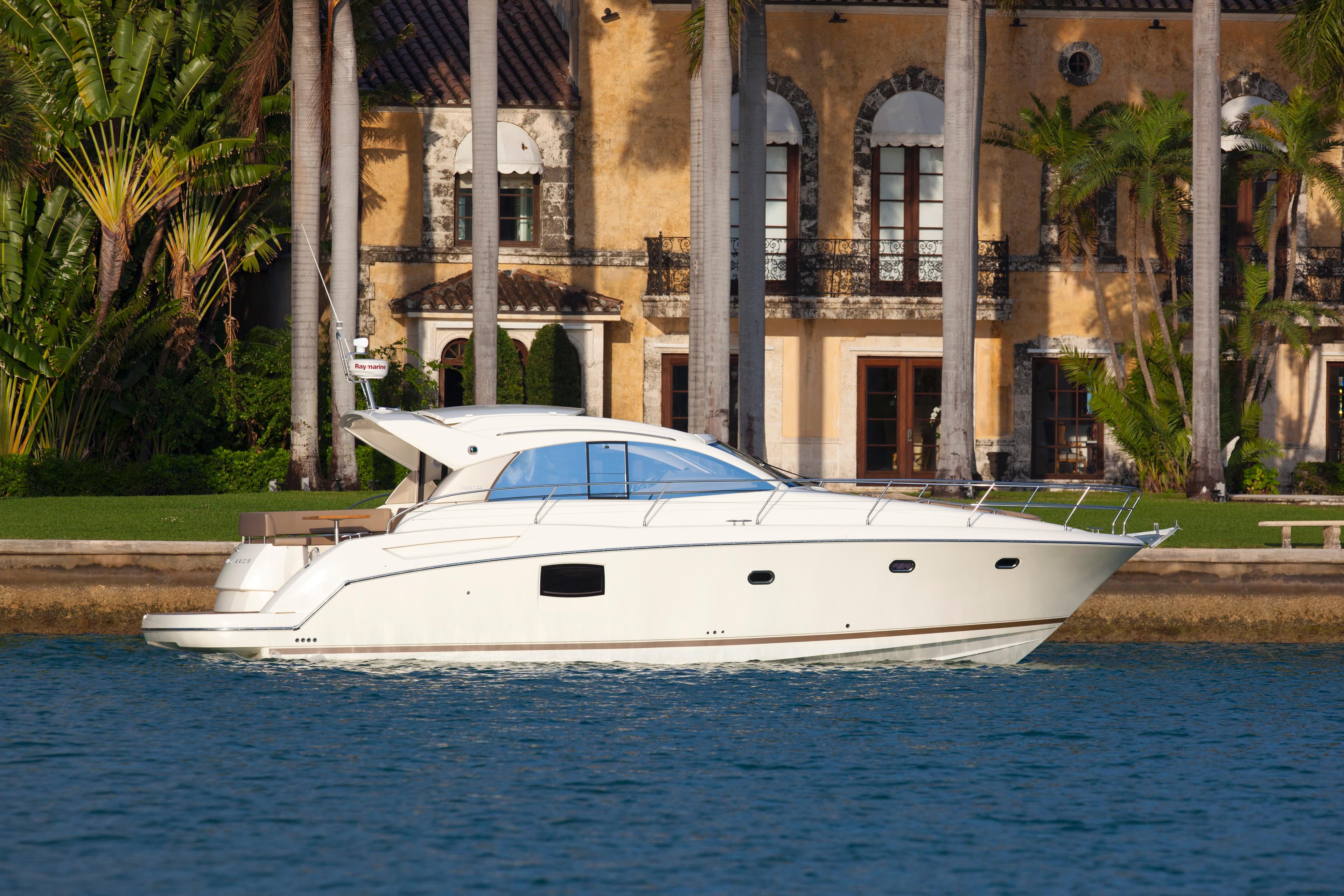 2012 Prestige 440S yacht cruising near a luxurious waterfront villa.