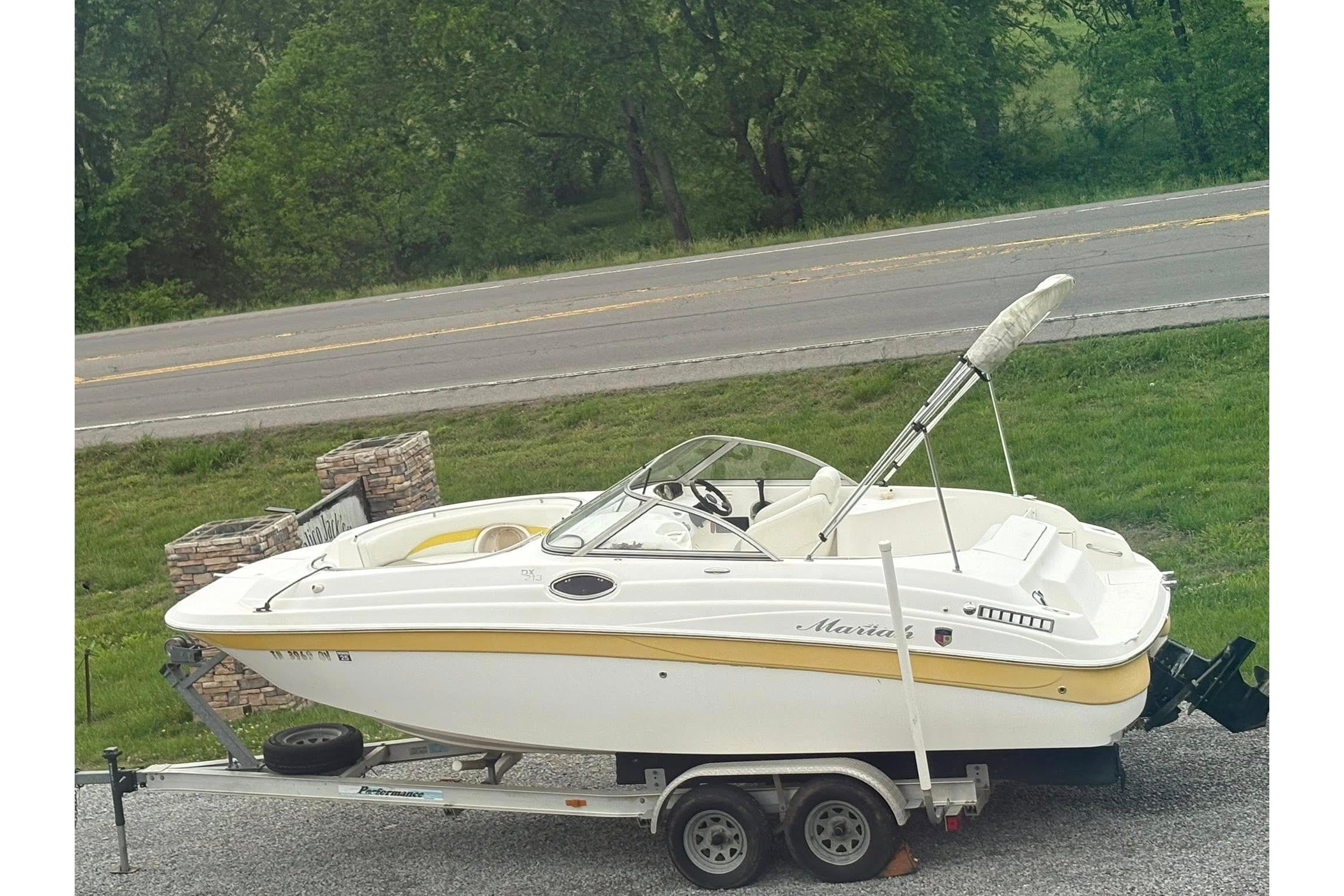 2004 Mariah DX213 boat on trailer, parked near a road with lush greenery.
