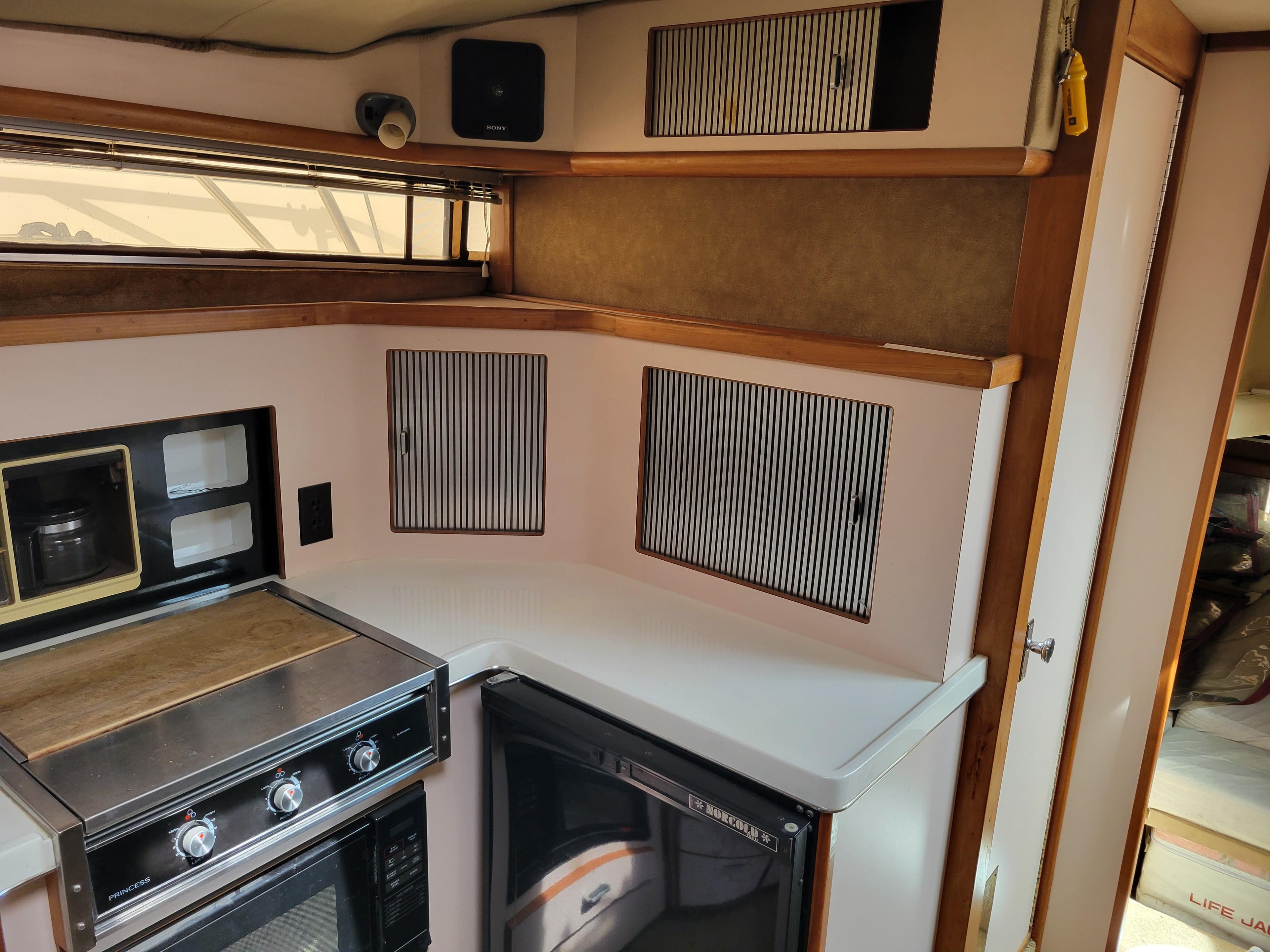 1989 Sea Ray 340 Sundancer kitchen with stove, cabinets, and compact fridge.