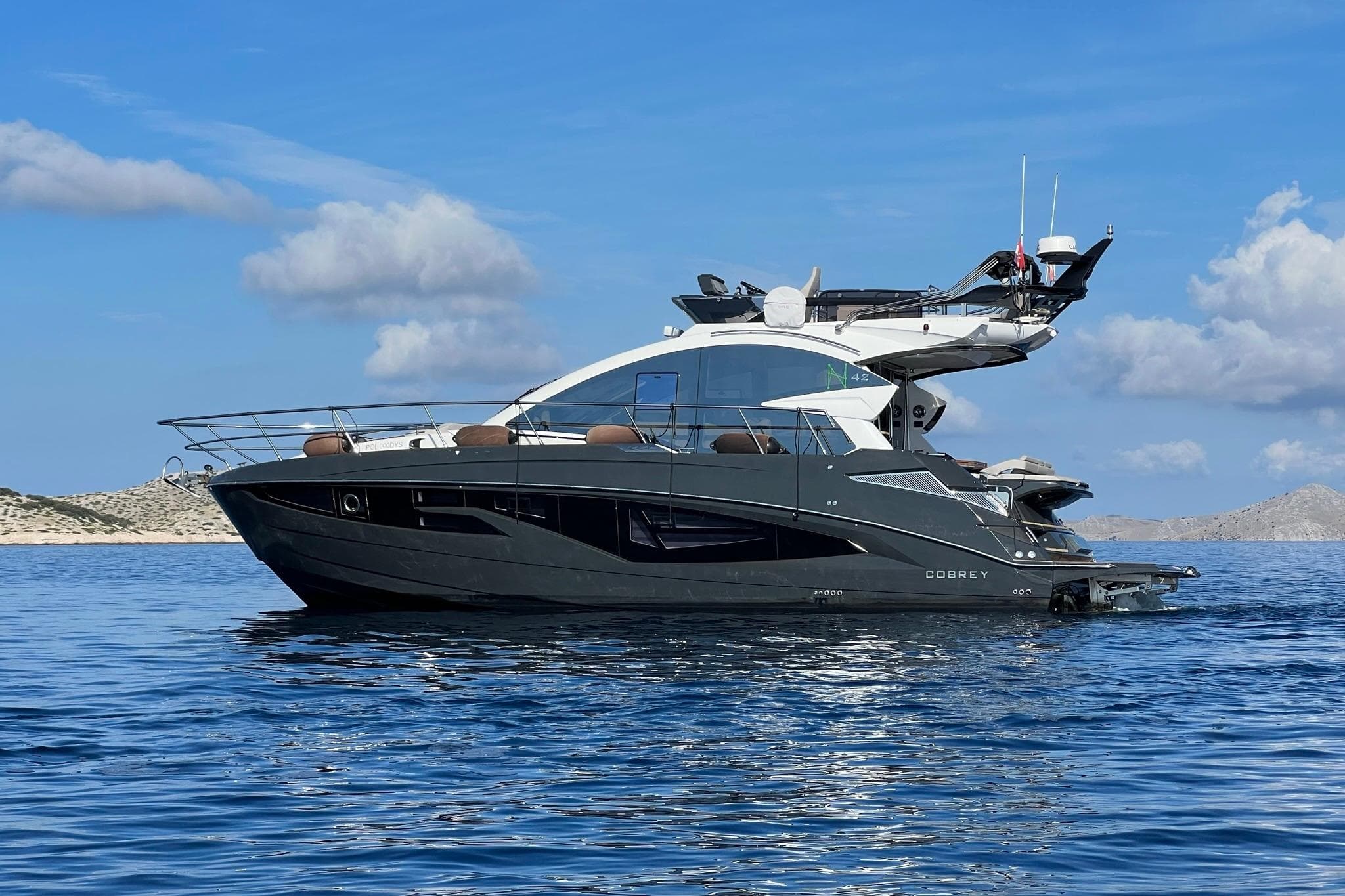 2026 Cobrey 45 FLY yacht on calm sea with scenic background.