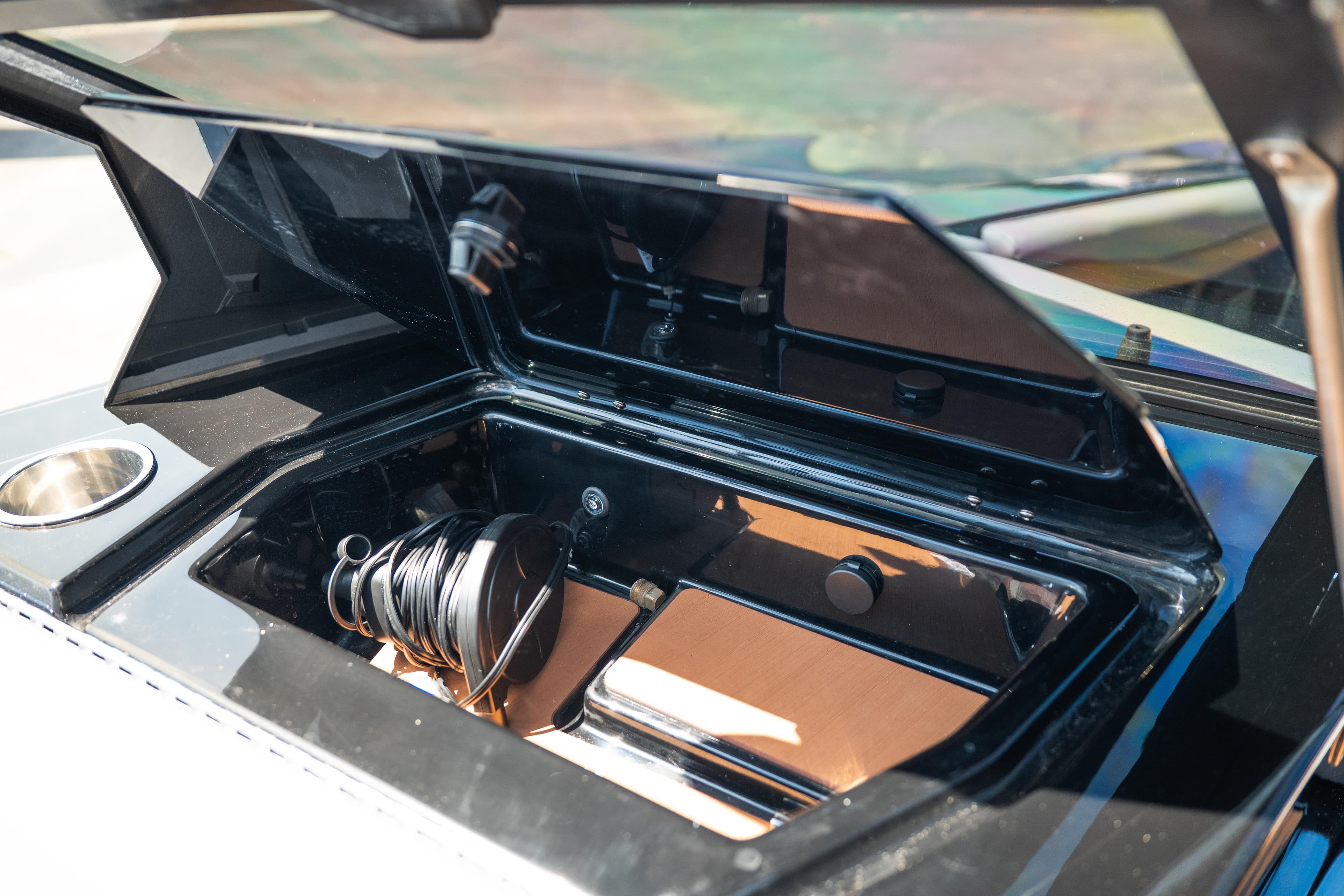 Open storage compartment in 2025 Axis A225 boat, featuring coiled cable and cup holder.