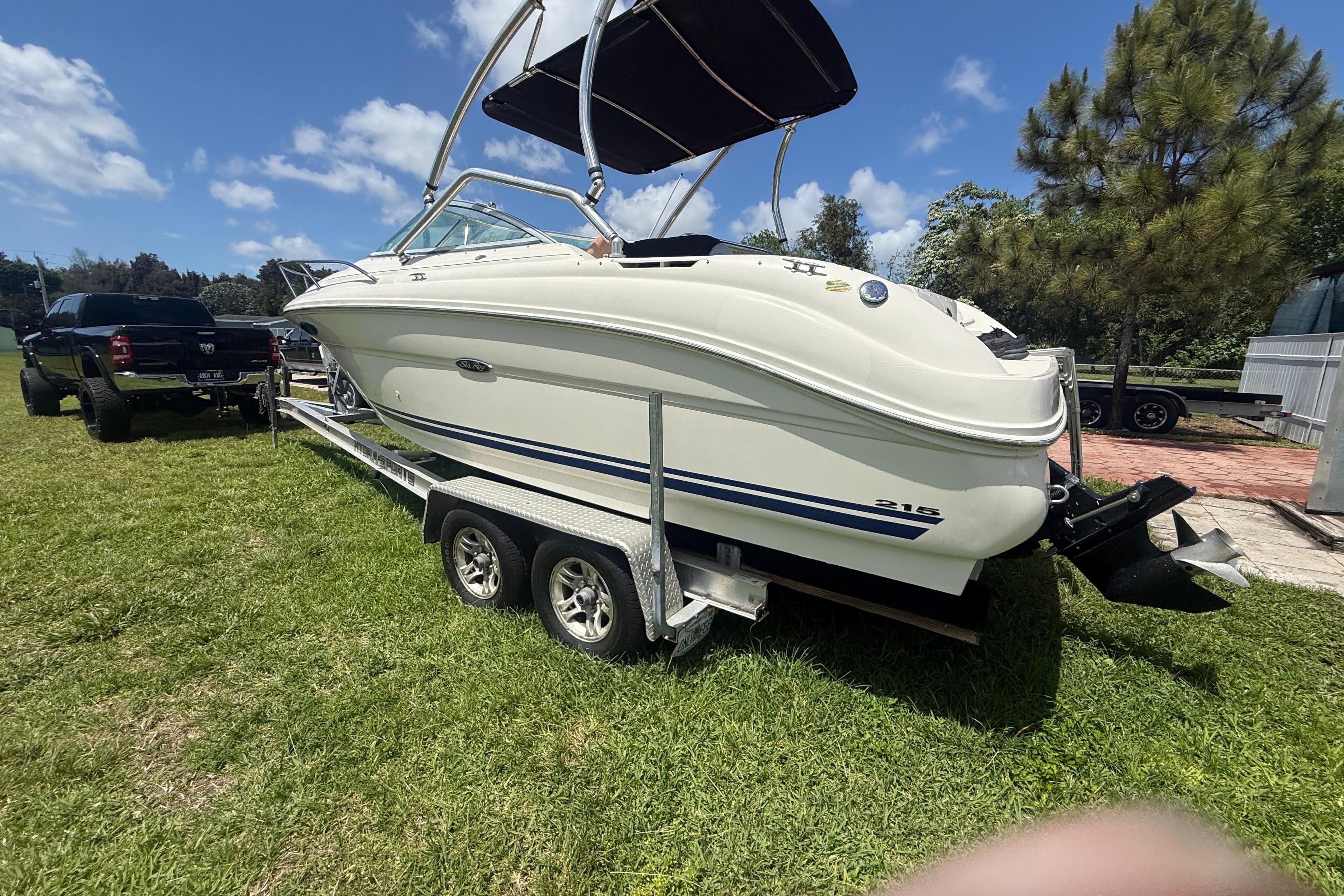2004 Sea Ray 215 Weekender boat on trailer, parked on grass under a clear blue sky.