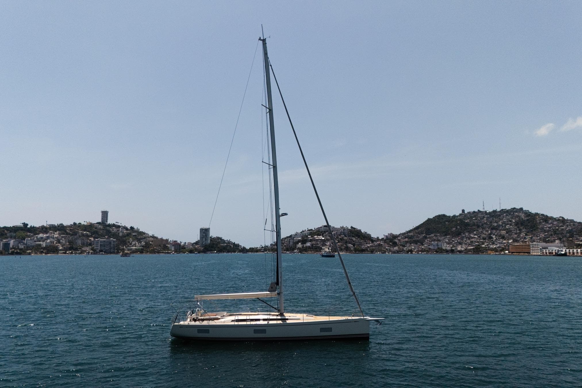 Sailing yacht Nautor Swan 55, 2023 model, on calm waters with hilly coastline backdrop.