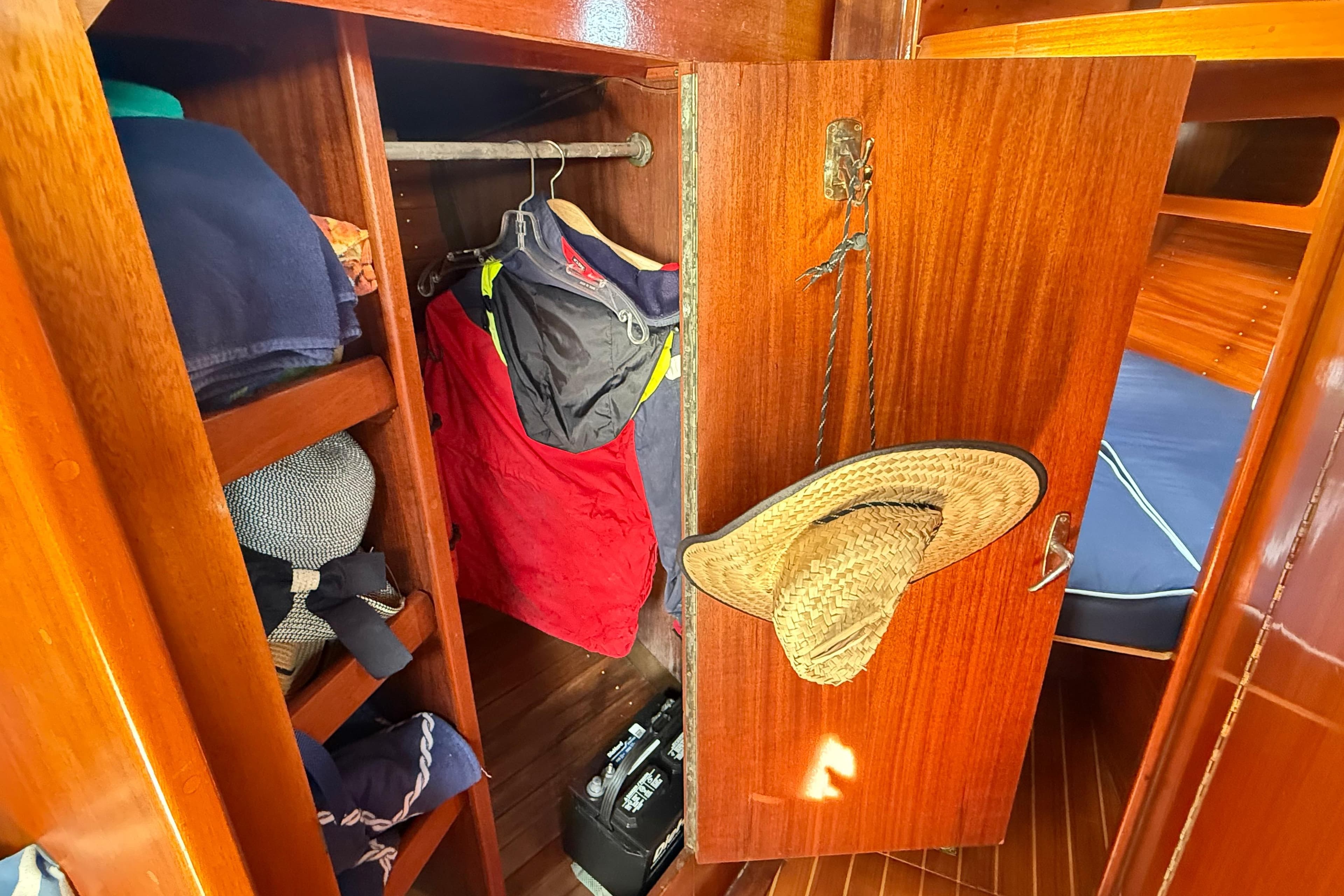 Wooden closet interior on a 1986 Vindo 45 sailboat, with clothes and a straw hat.
