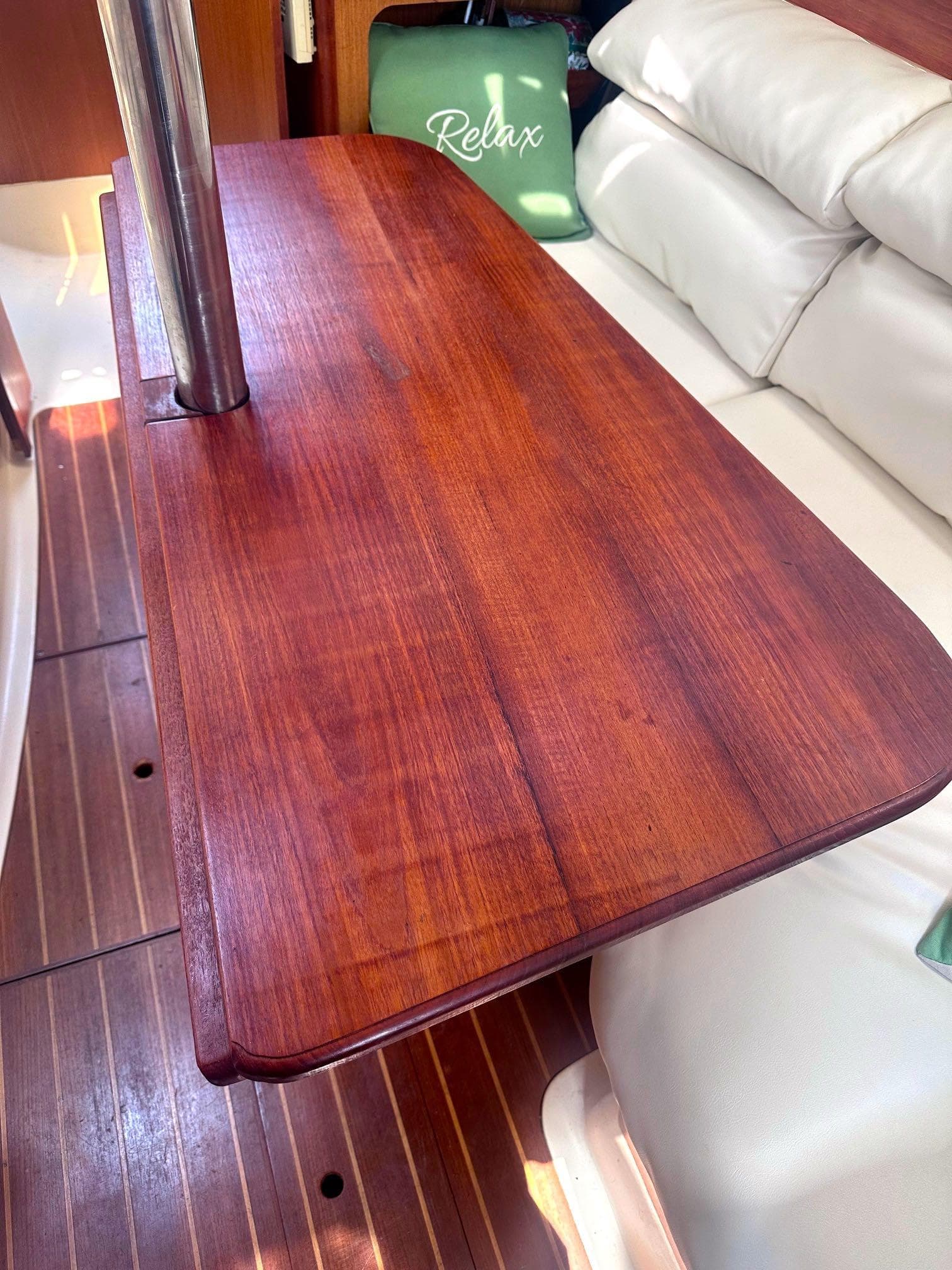 Wooden table inside a 1997 Hunter 310 sailboat, with white seating and a "Relax" pillow.