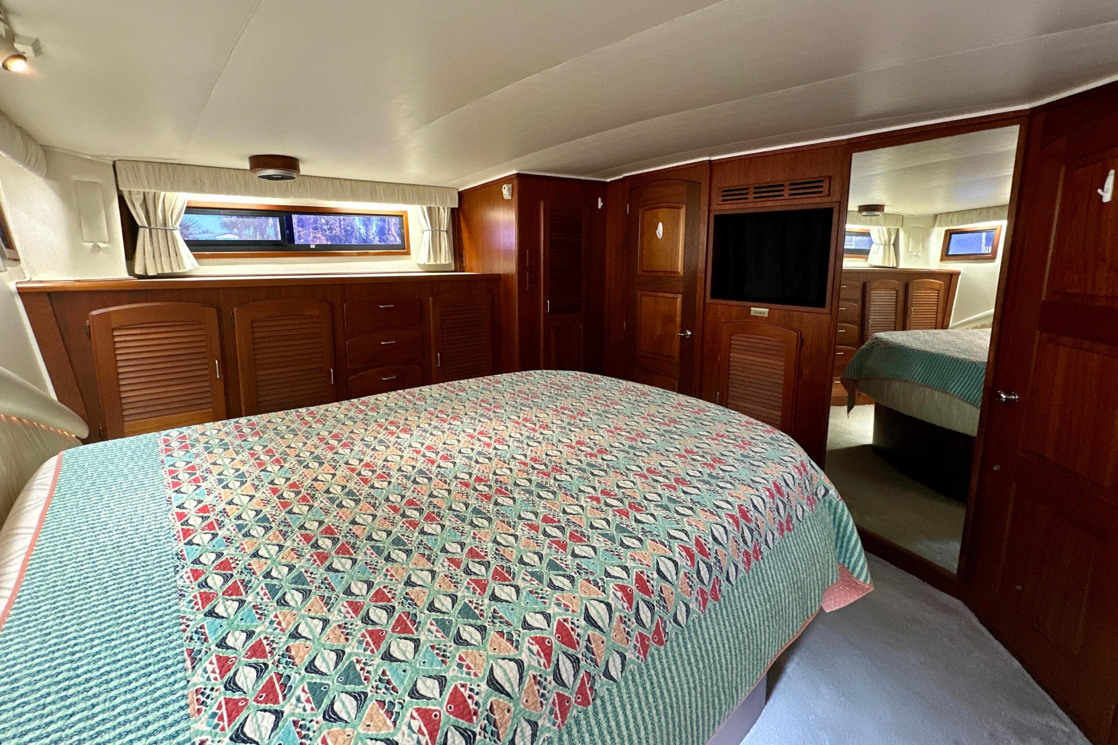 Luxurious bedroom interior of 1988 Californian 45 Motor Yacht with patterned bedding and wooden cabinetry.
