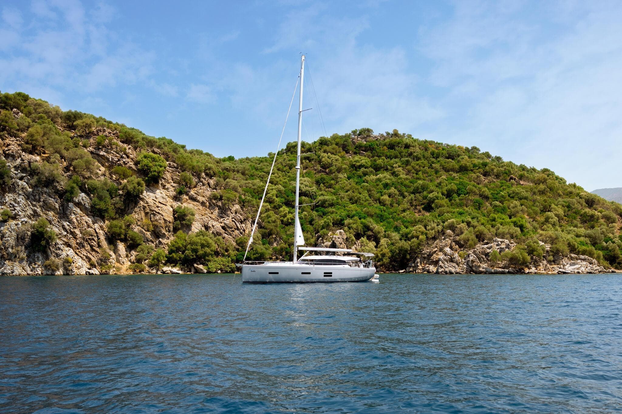 2026 Moody Decksaloon 48 yacht sailing near lush, rocky coastline.