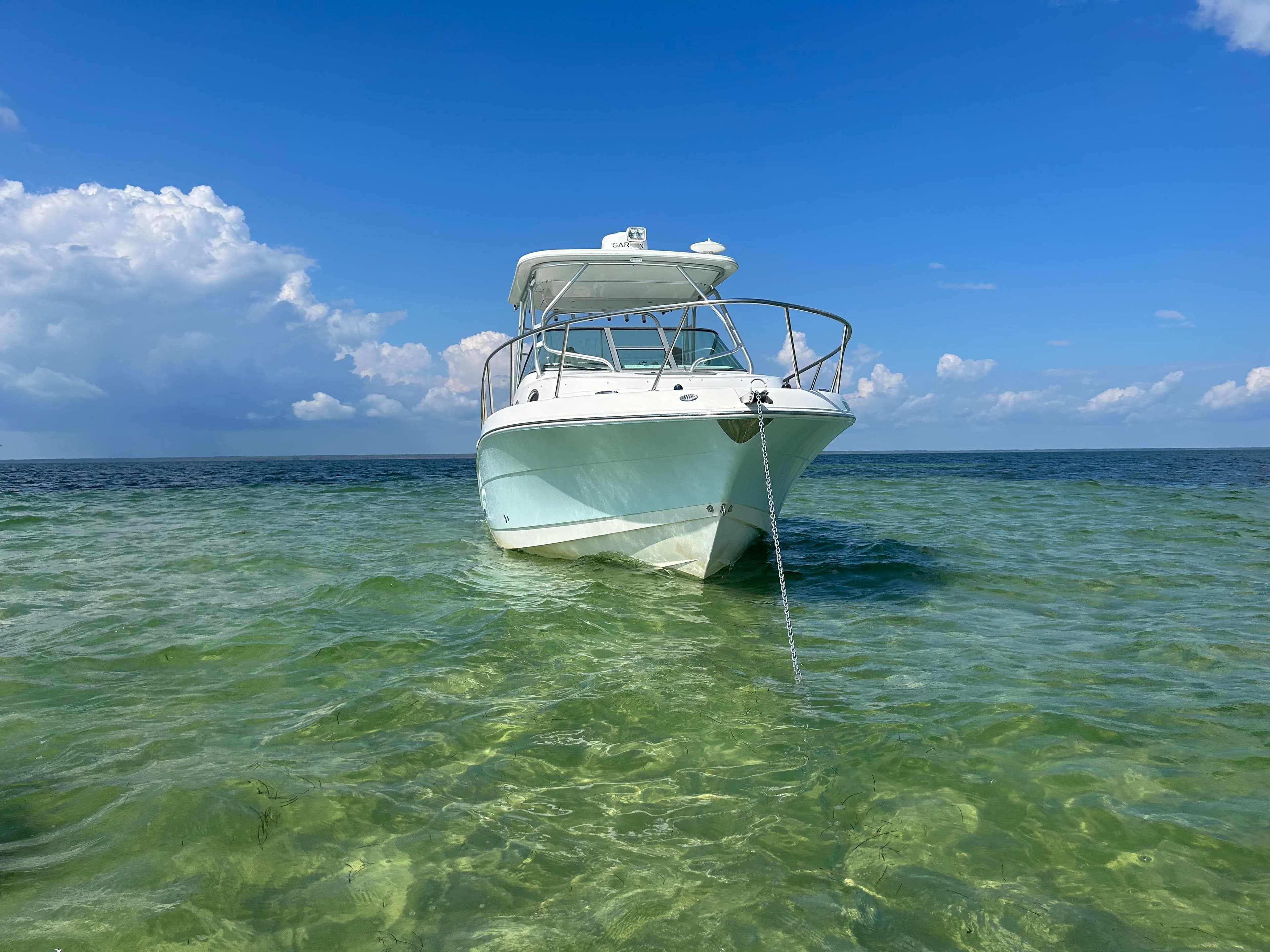 2015 Robalo R305 Walkaround boat anchored in clear, shallow water under a blue sky.