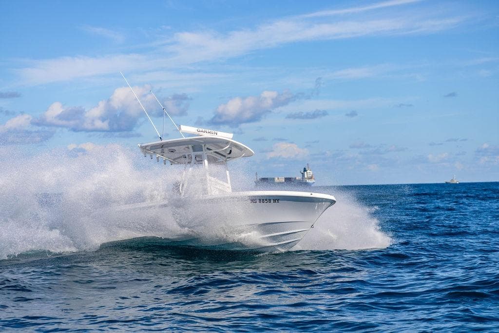 2024 Reef Runner 230 Open boat cruising on ocean waves under a clear blue sky.