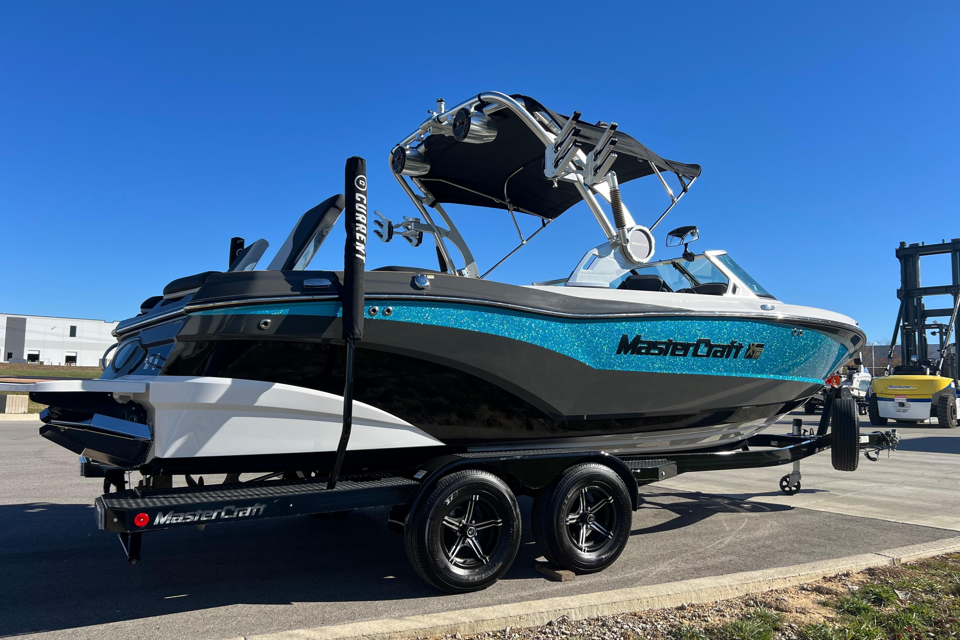 2020 MasterCraft XT23 boat on trailer, vibrant blue and black design, clear sky background.