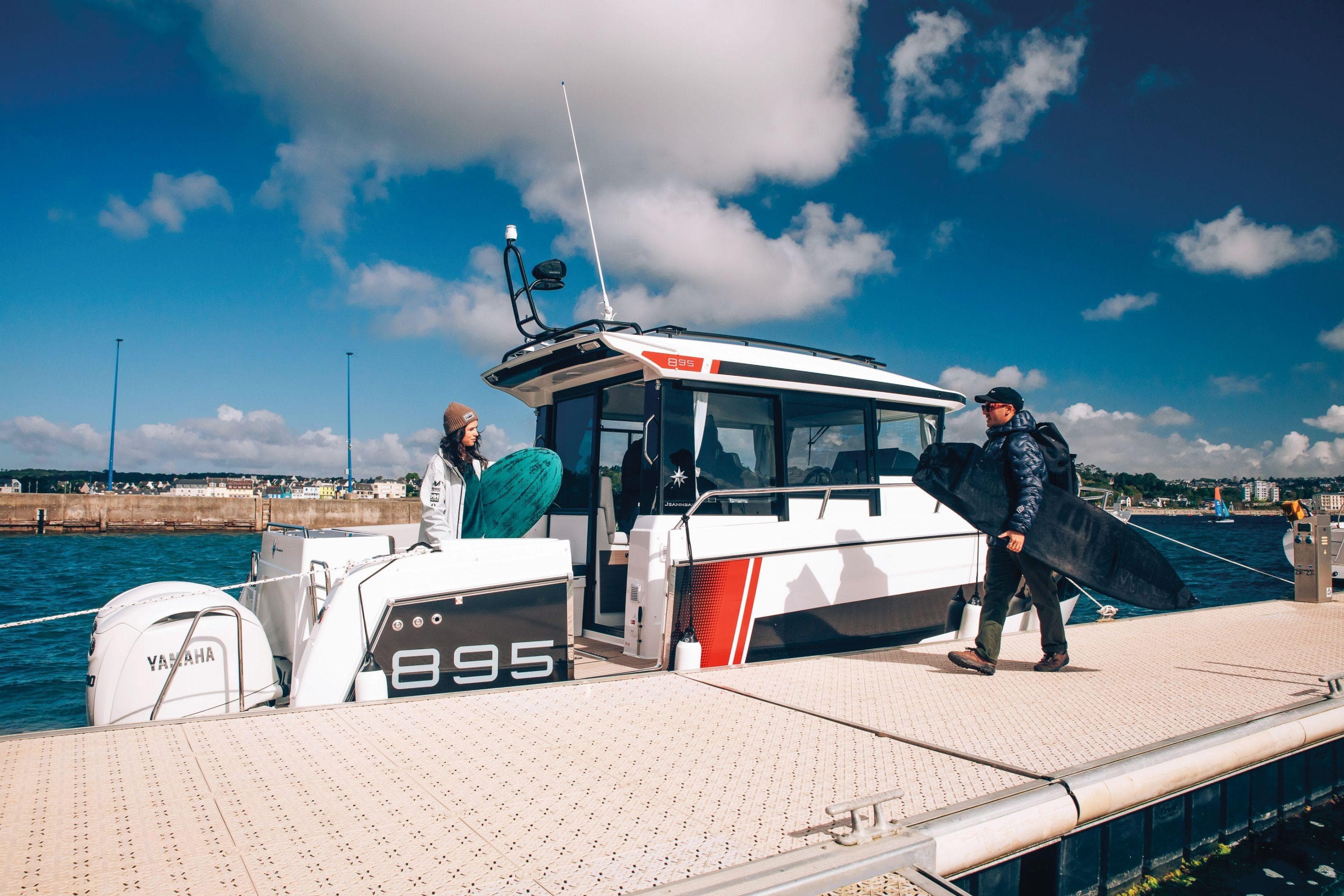 2026 Jeanneau NC 895 Sport Series 2 docked, with people carrying surfboards.