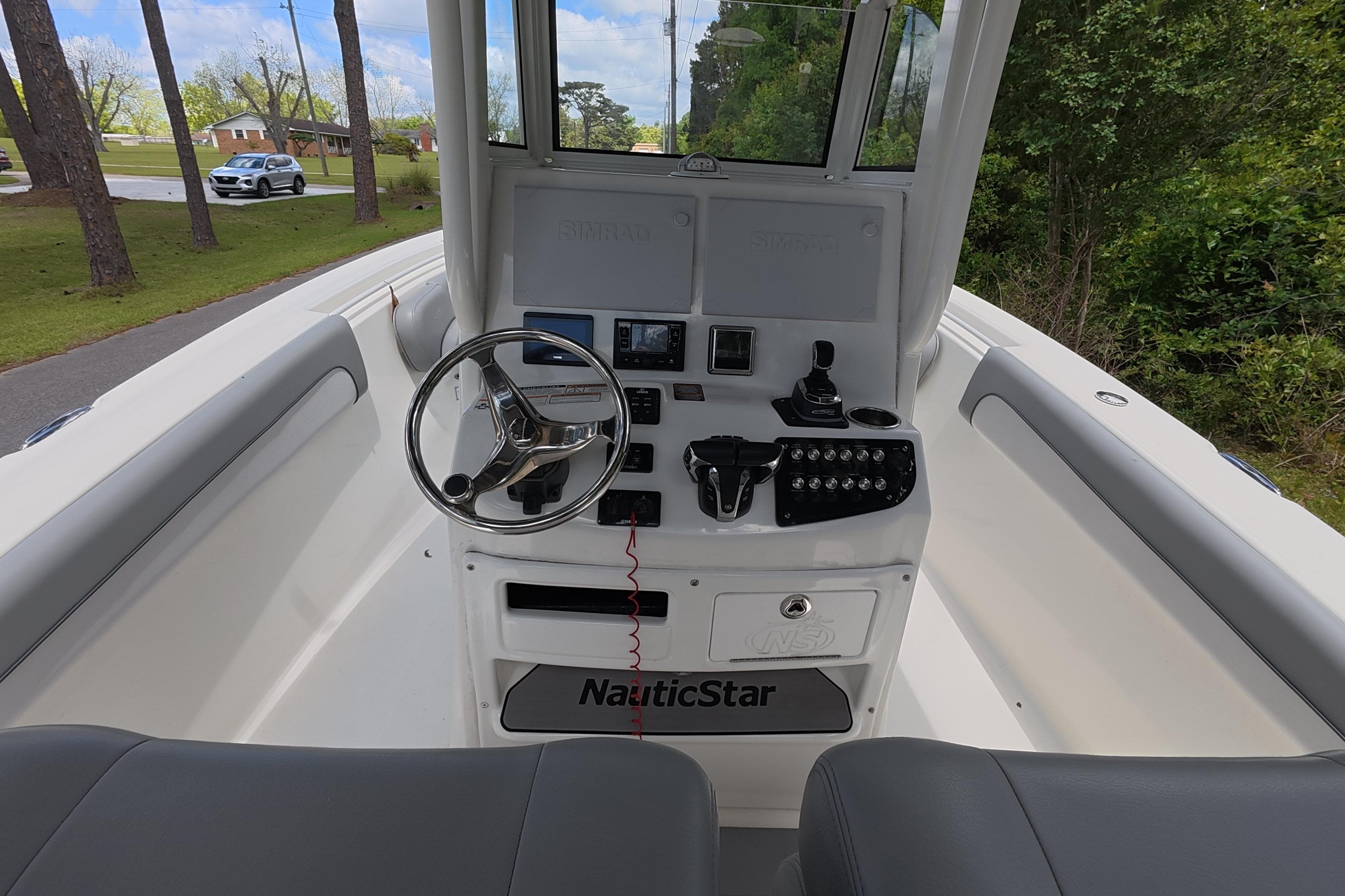 2021 NauticStar 28 XS boat console with steering wheel and controls, surrounded by lush greenery.