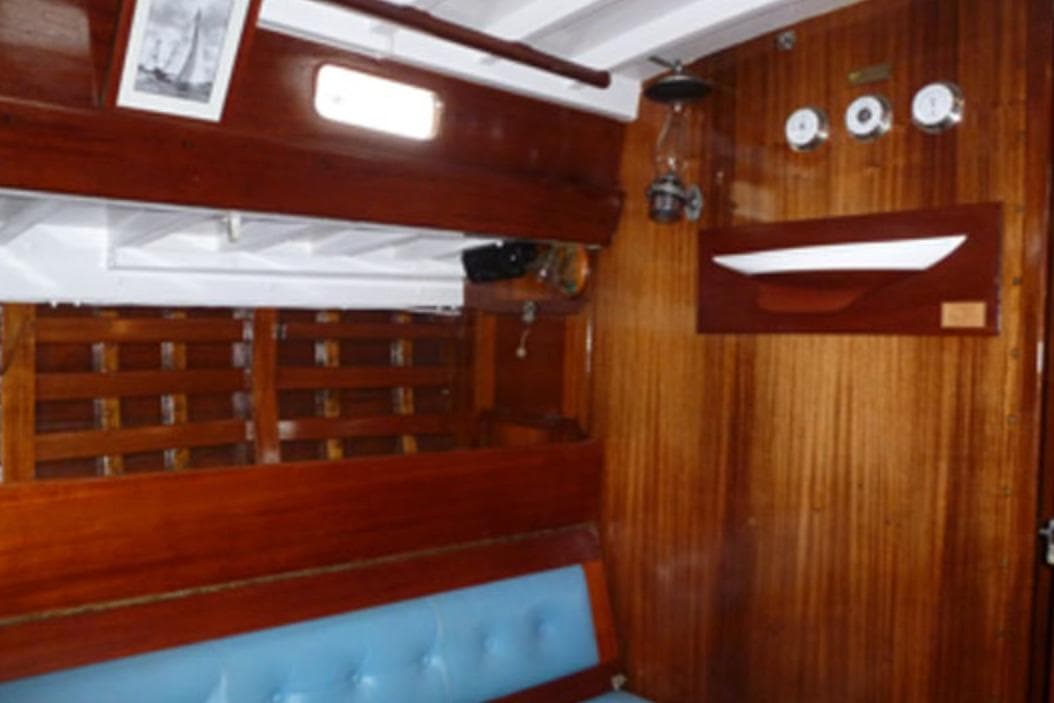 Interior of a 1959 McGruer Bermudian yawl with wooden paneling and blue seating.