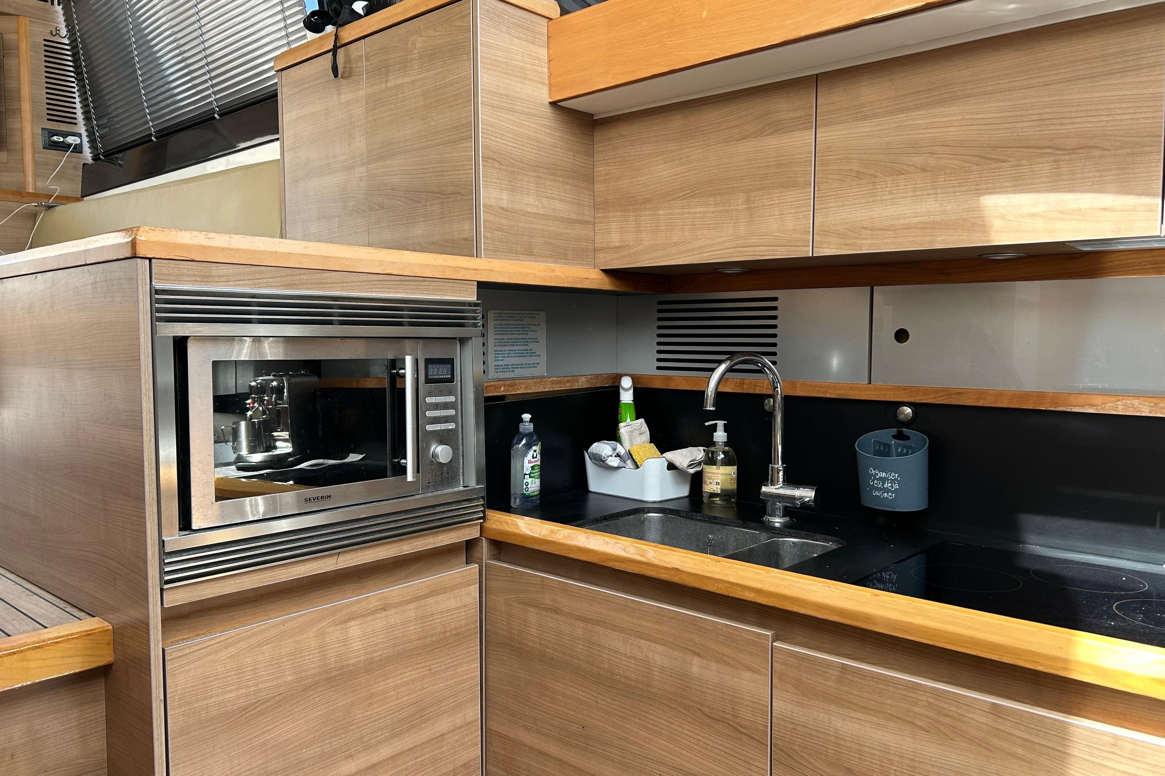 Modern kitchen interior on a 2012 Sealine F42 yacht, featuring wood cabinetry and stainless steel appliances.