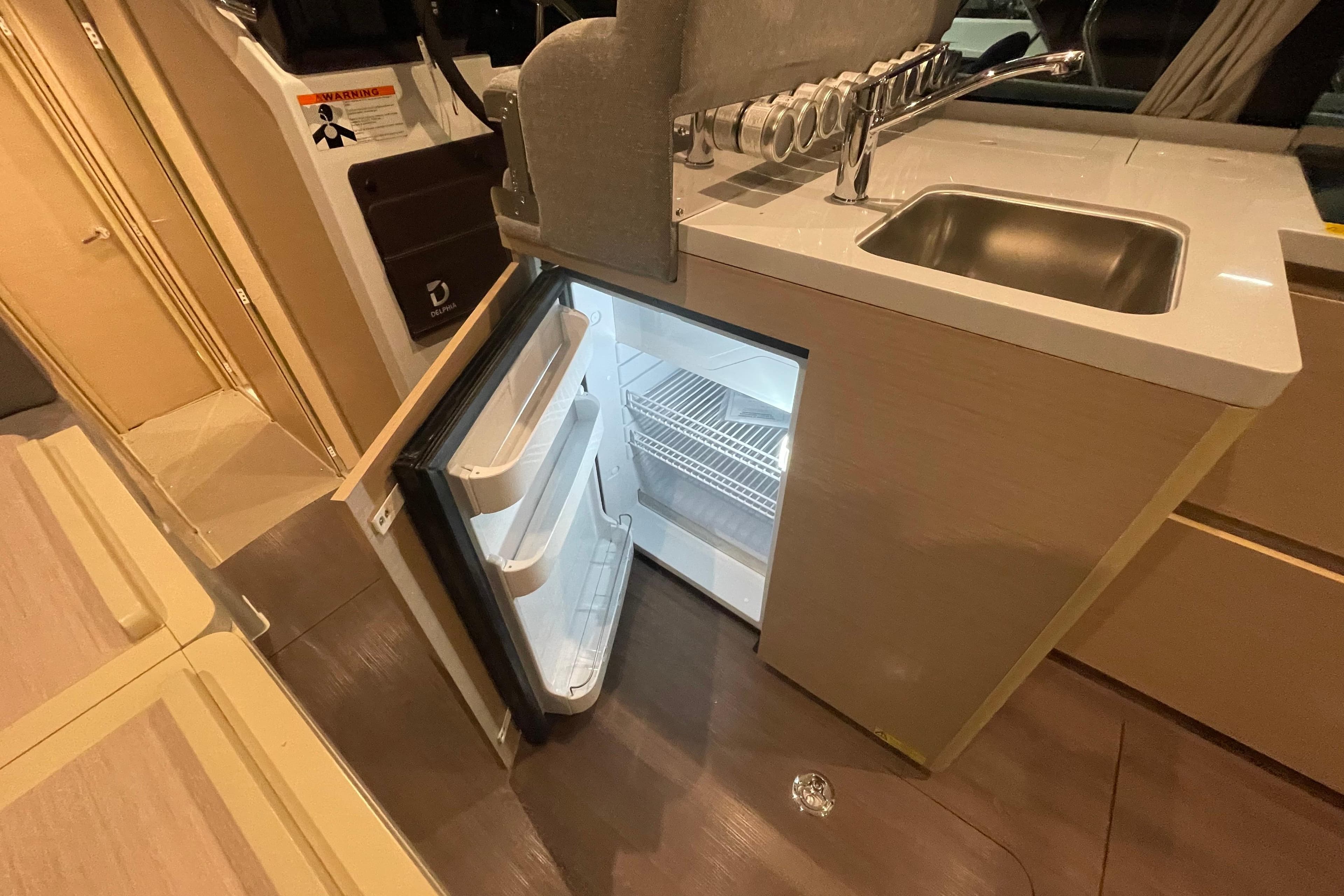 Compact kitchen area in 2025 Delphia 11 Sedan with open fridge and sink.